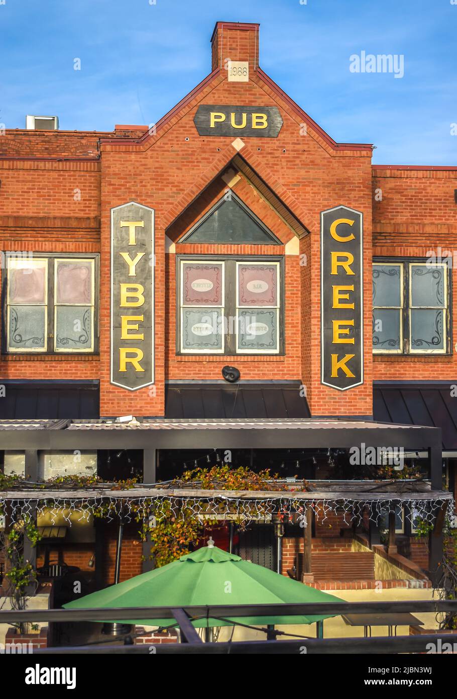 La facciata esterna del Tyber Creek Pub e la segnaletica con logo con cielo blu, finestre in vetro riflettente, patio e ombrello verde a Charlotte, NC. Foto Stock