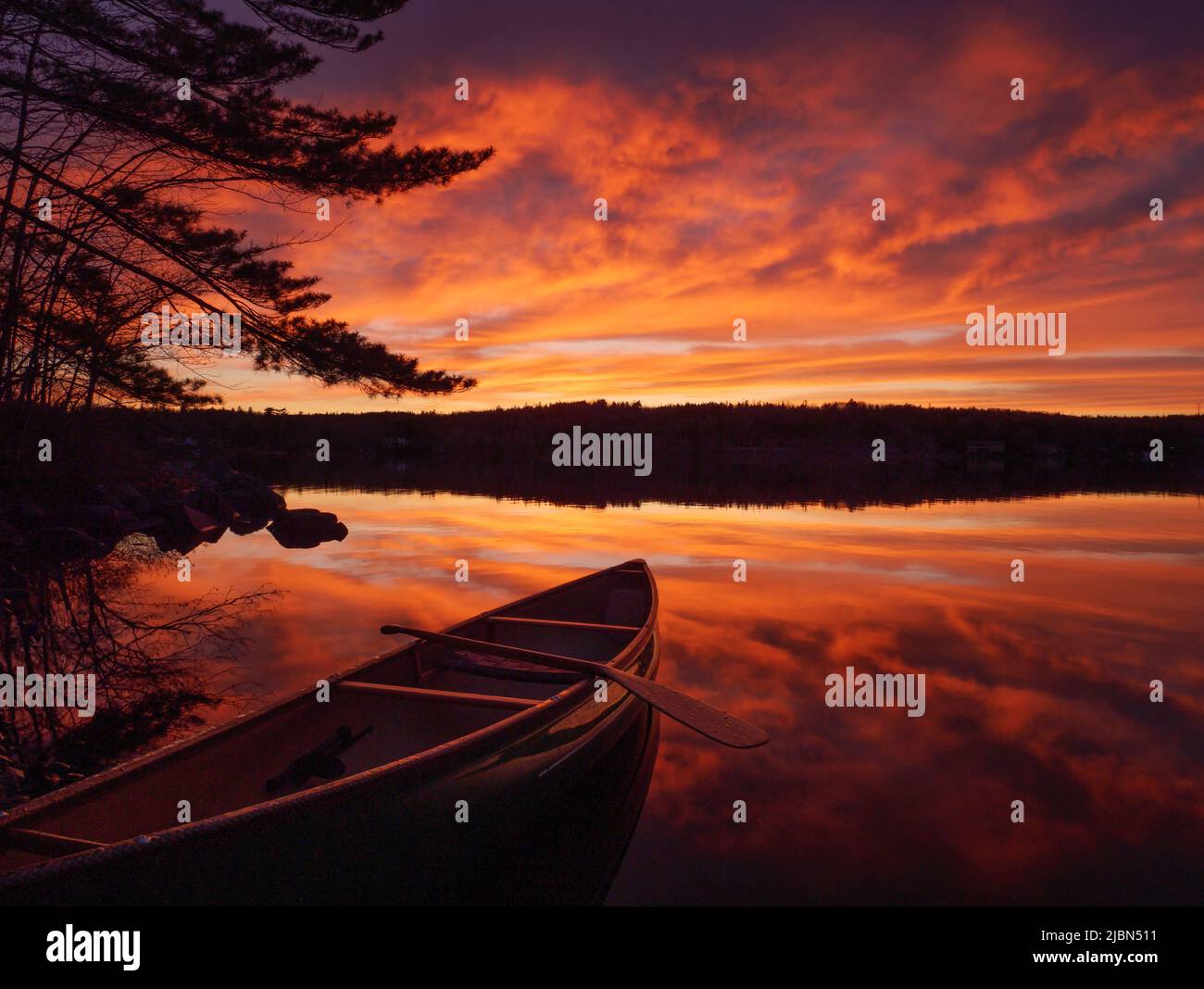 Una piccola barca sul lato del lago al tramonto con un suggestivo sfondo del cielo di colore rosso Foto Stock