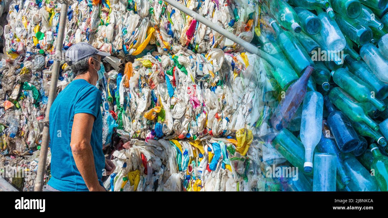 Uomo che guarda contenitori di plastica compressa con bottiglie di vetro sovrastate. Plastica, riciclaggio del vetro, consumismo, riscaldamento globale, inquinamento Foto Stock