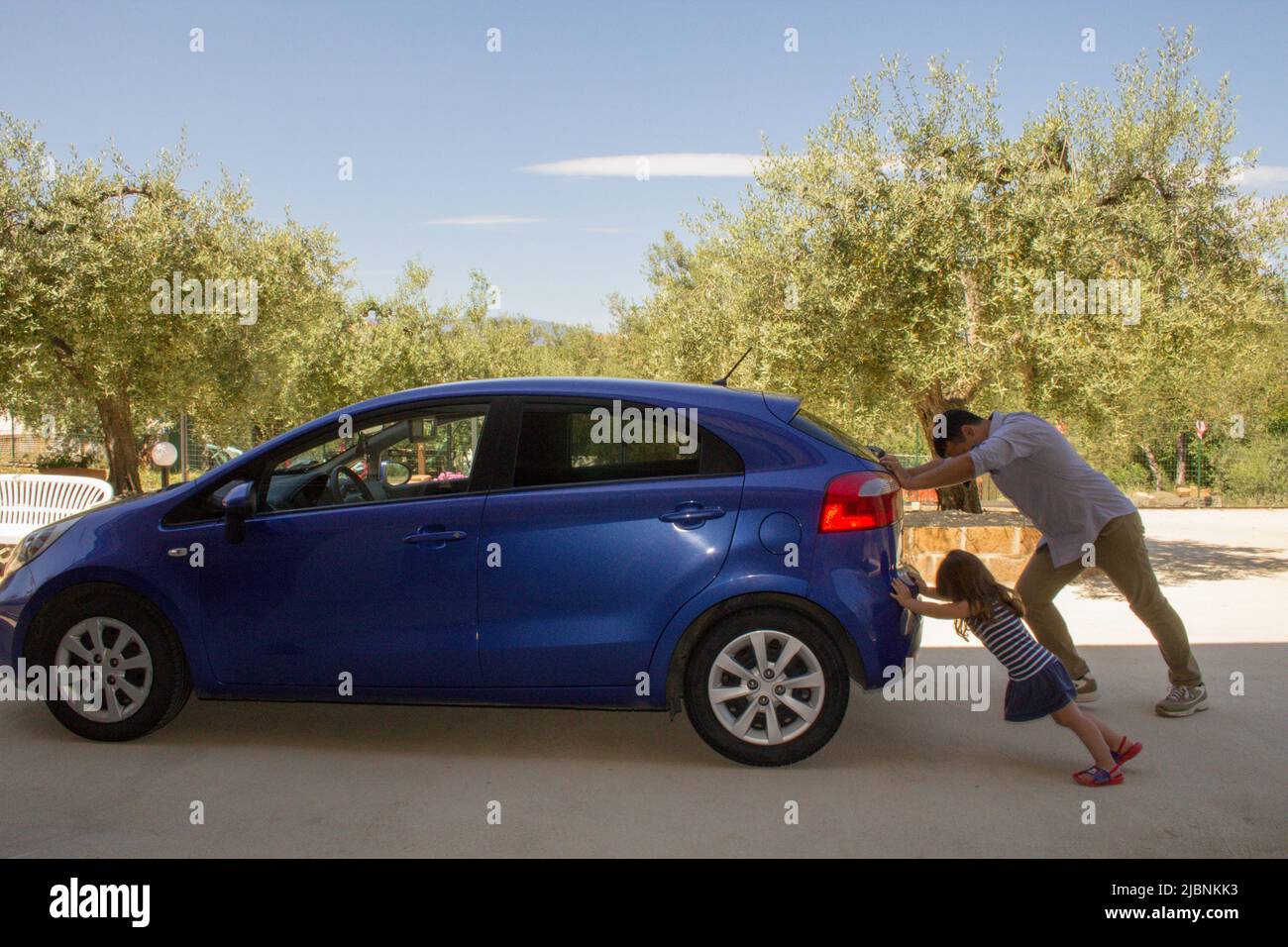 immagine di un uomo che con la figlia spinge la propria auto dopo aver avuto un guasto e la benzina. Riferimento all'attuale carburante costoso Foto Stock