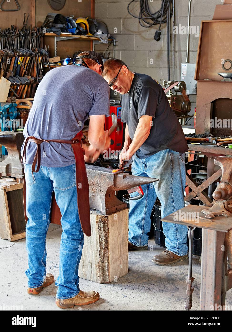 Due uomini usano un martello e l'incudine per formare il ferro caldo in una lama del coltello all'azienda dell'artigianato del metallo della montagna di ferro a Pigeon Forge Tennessee, Stati Uniti. Foto Stock