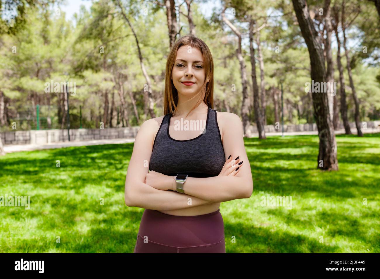 Bella donna bruna con reggiseno sportivo in piedi sul parco cittadino, all'aperto faccia felice sorridente con braccia incrociate che guardano via con sicura espressio Foto Stock