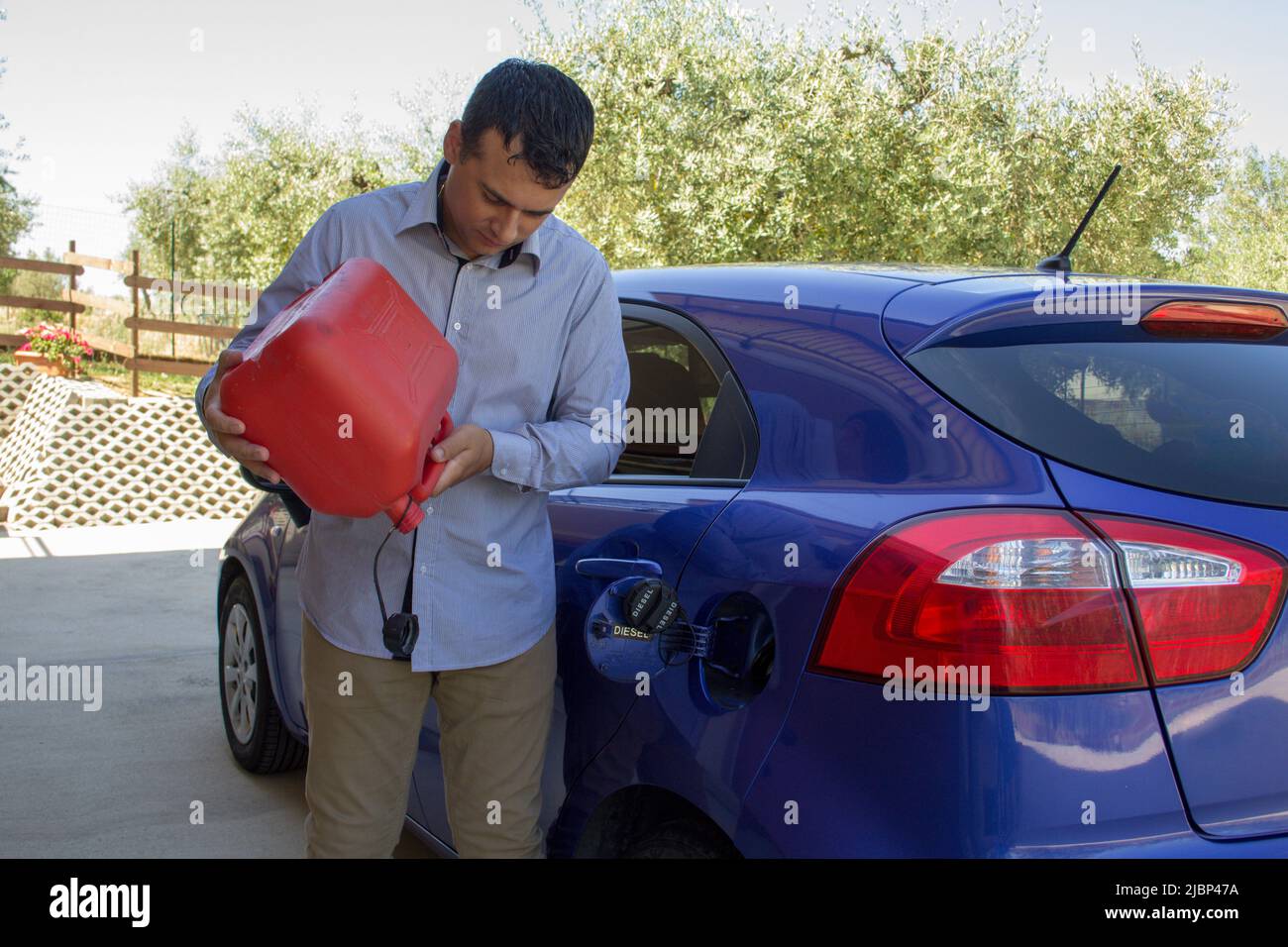 Immagine di un uomo che tiene una bomba di benzina vuota con il serbatoio della sua auto aperto. Riferimento a carburante costoso Foto Stock