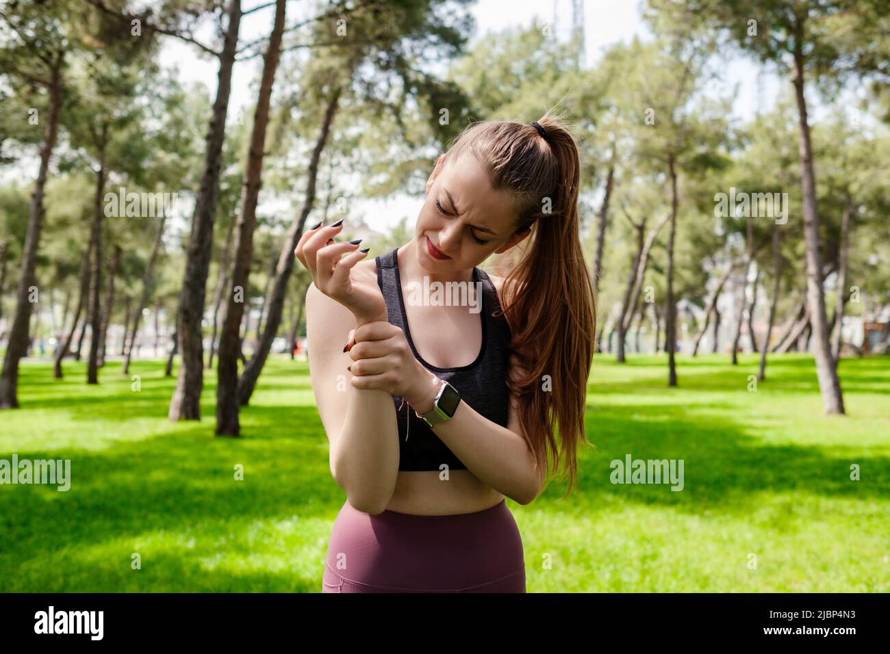Ritratto di donna bruna con reggiseno sportivo in piedi sul parco della città, all'aperto tenendo il suo polso doloroso. Dolore alle mani e alle dita, artriti Foto Stock