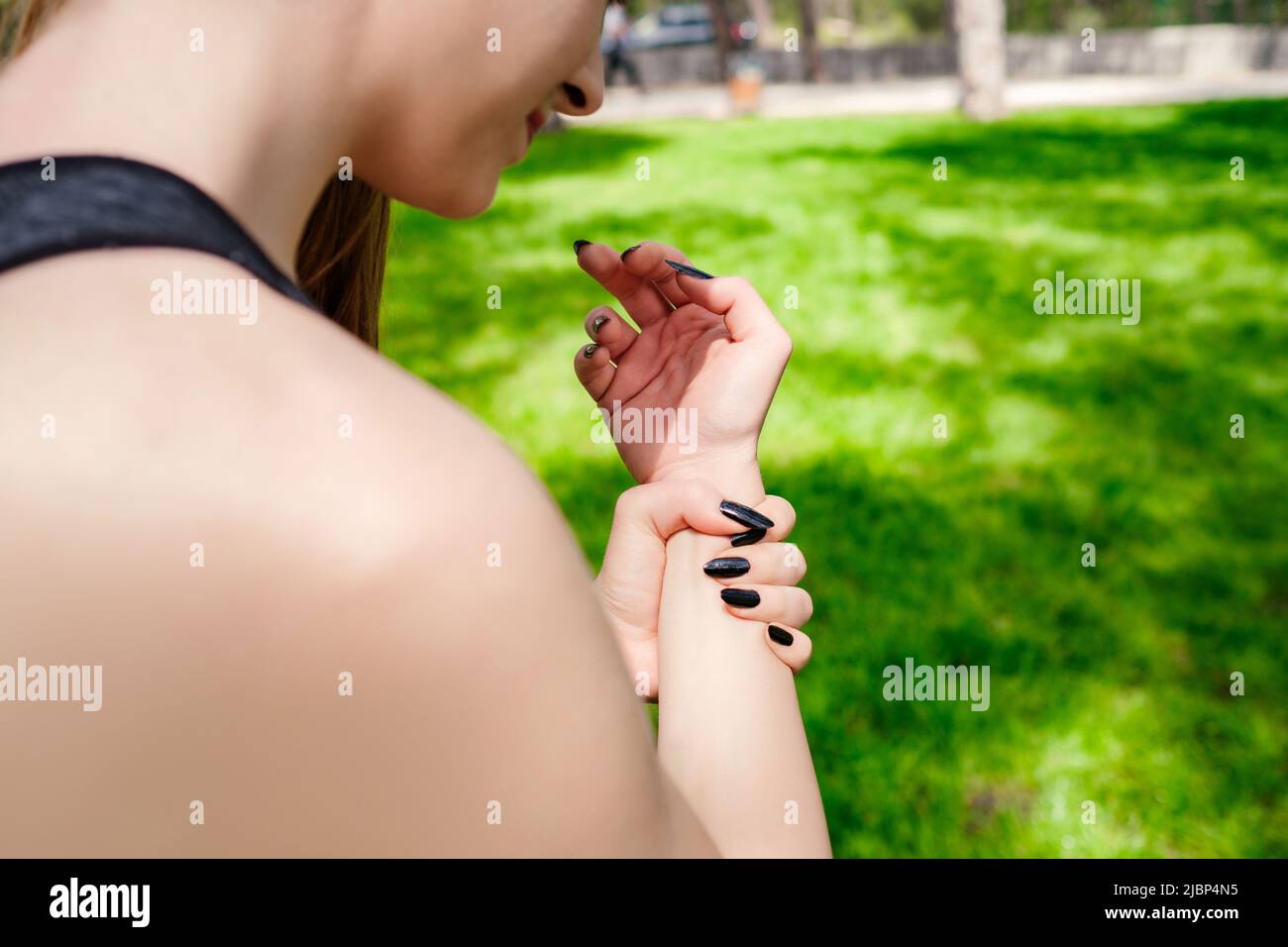 Giovane donna bruna che indossa abiti sportivi sul parco cittadino, all'aperto tenendo il suo polso doloroso. Dolore alle mani e alle dita, infiammazione dell'artrite Foto Stock