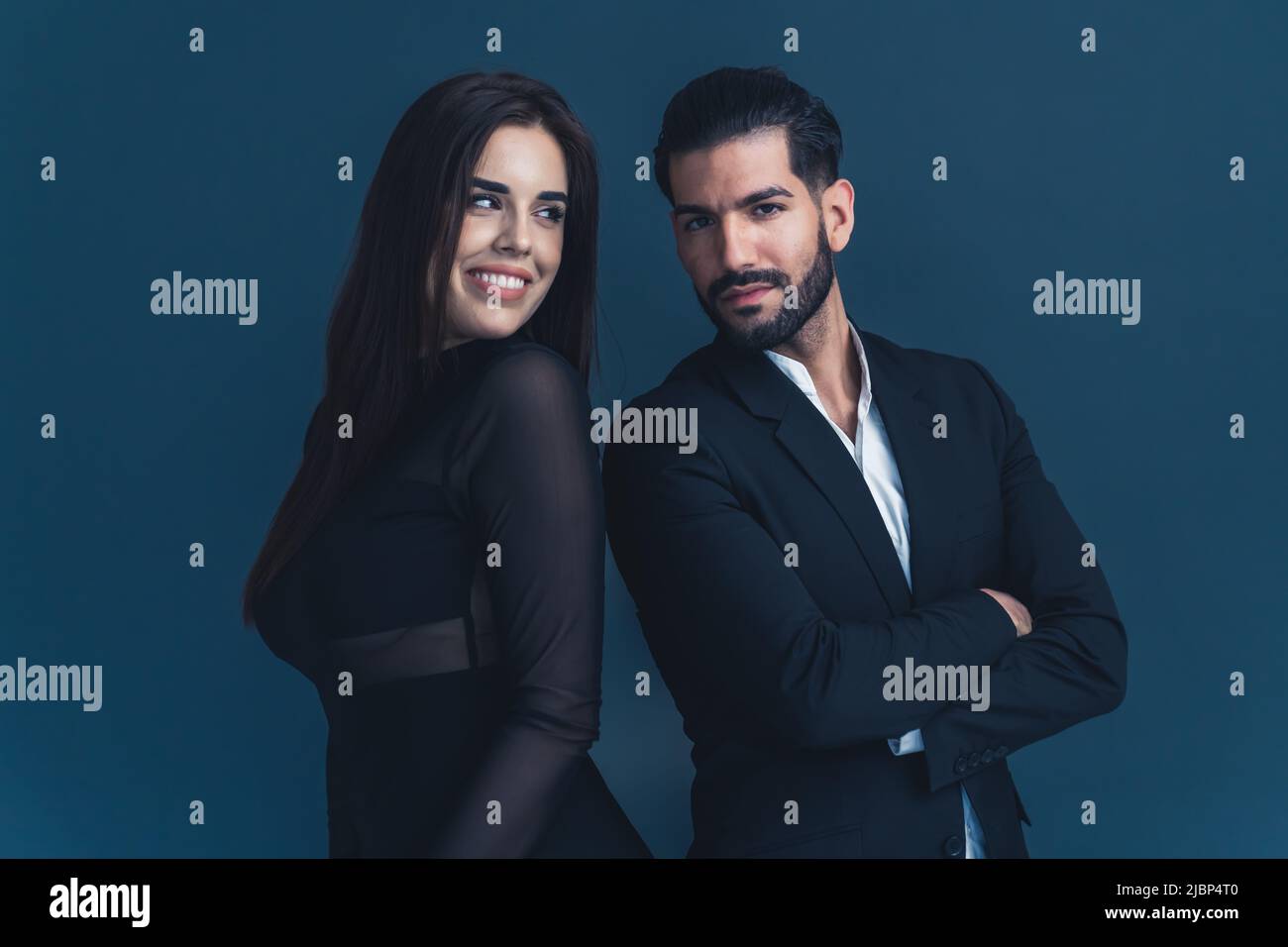 Due professionisti in ufficio. Bella donna d'affari dai capelli lunghi e bel uomo d'affari in un vestito in piedi indietro in uno studio su sfondo scuro. Foto di alta qualità Foto Stock