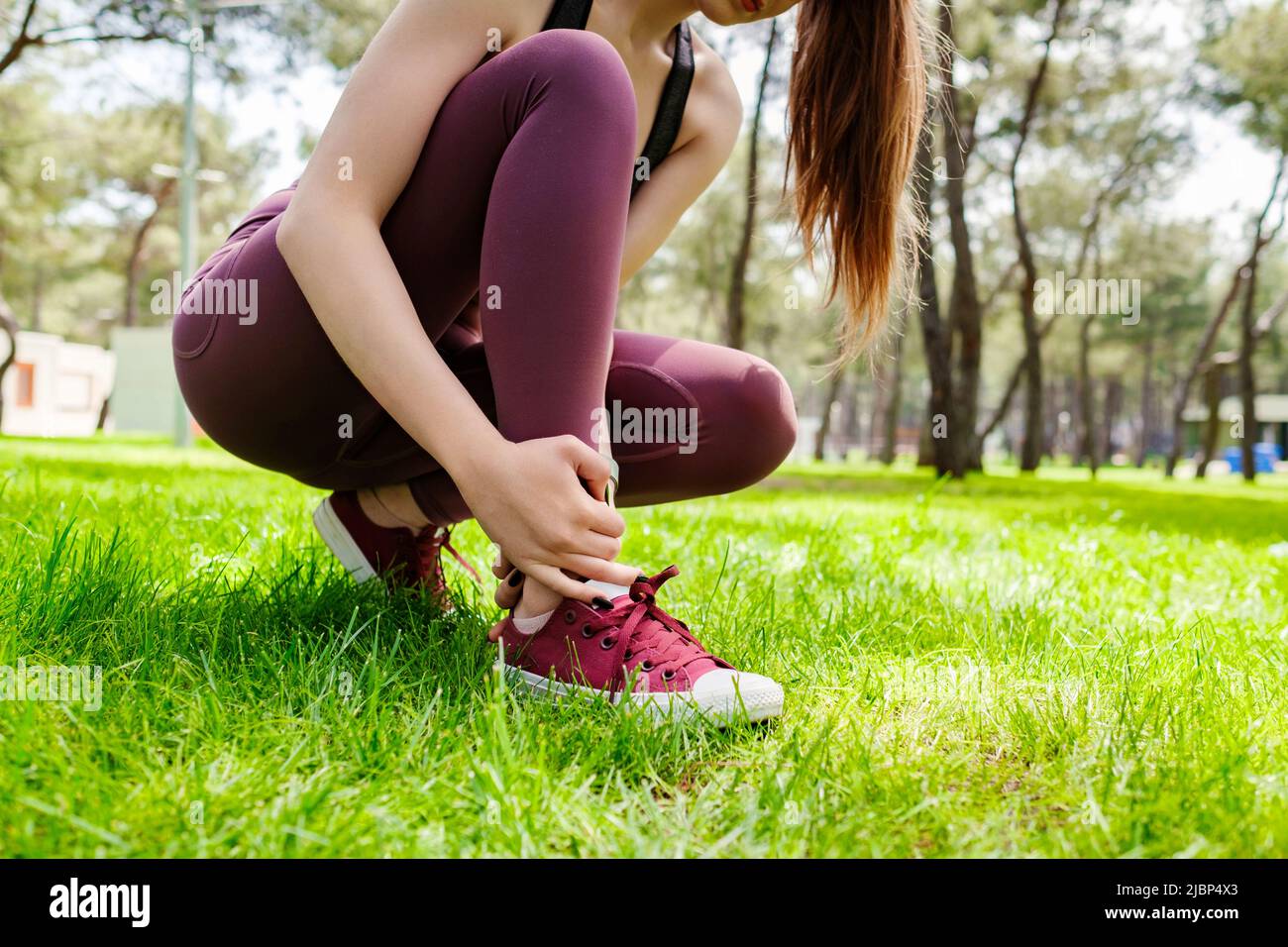 Bella donna bruna con reggiseno sportivo in piedi sul parco della città, all'aperto che soffre di una lesione alla caviglia durante l'esercizio e la corsa. Assistenza sanitaria e Foto Stock
