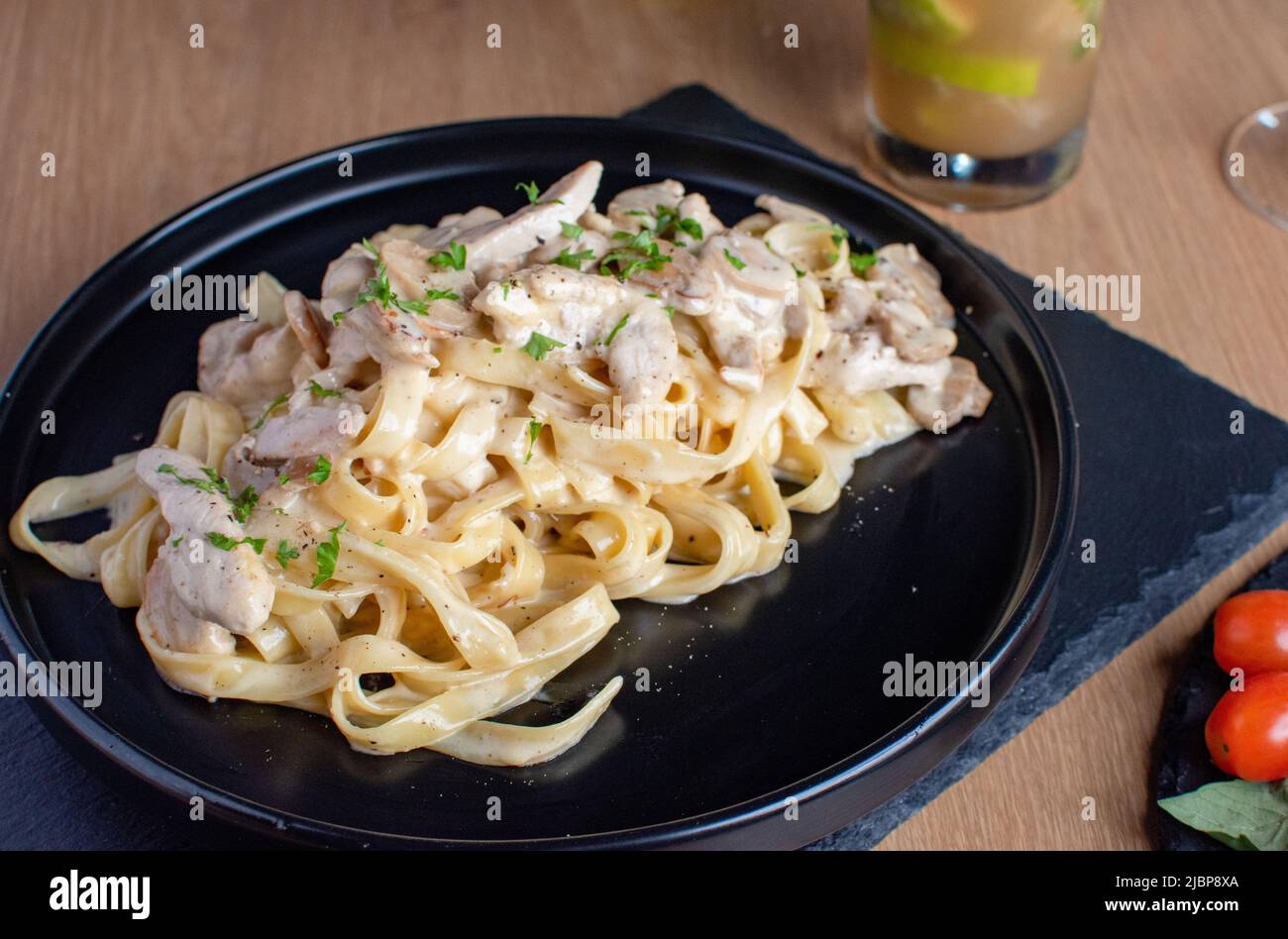 Pasta di pollo Alfredo con salsa bianca in un piatto nero Foto Stock