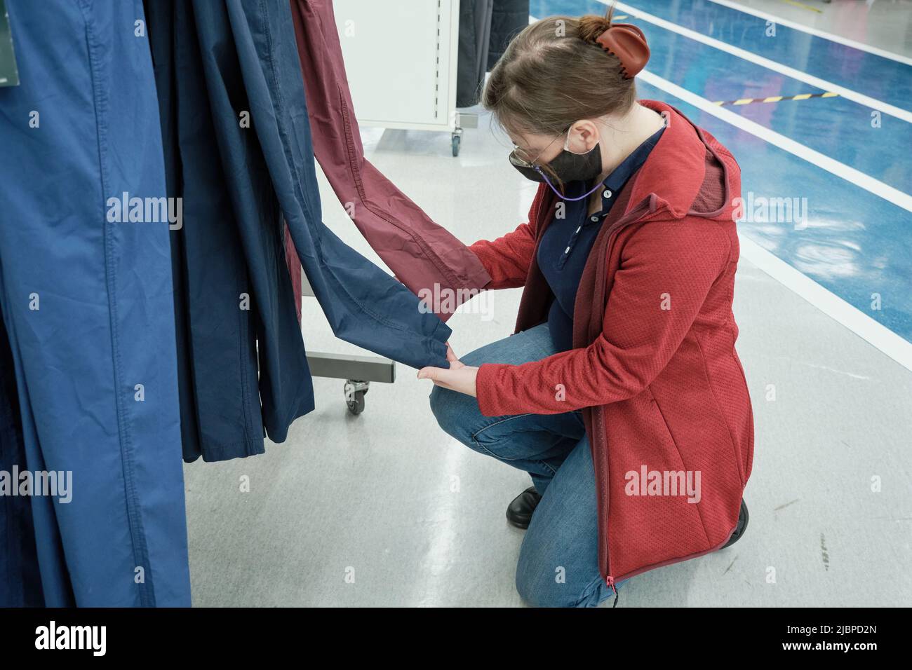 Donna in maschera contro il virus sceglie blu scuro e rosso pantaloni in negozio di abbigliamento Foto Stock