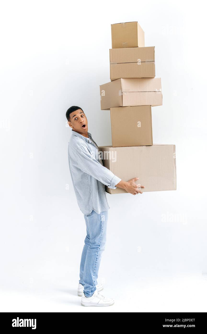 Stordito uomo di gara misto in abiti casual elegante, uomo di consegna, in piedi su fondo bianco isolato, tenere molte scatole di cartone, consegnare pacchi, guardare in stupore fotocamera, consegna Foto Stock