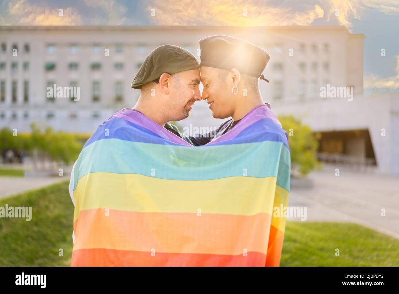 Coppia di gay innamorati abbracciati, avvolti da una bandiera gay, in un parco al tramonto, con riflessi del sole. Concetto di diversità, orgoglio, Foto Stock