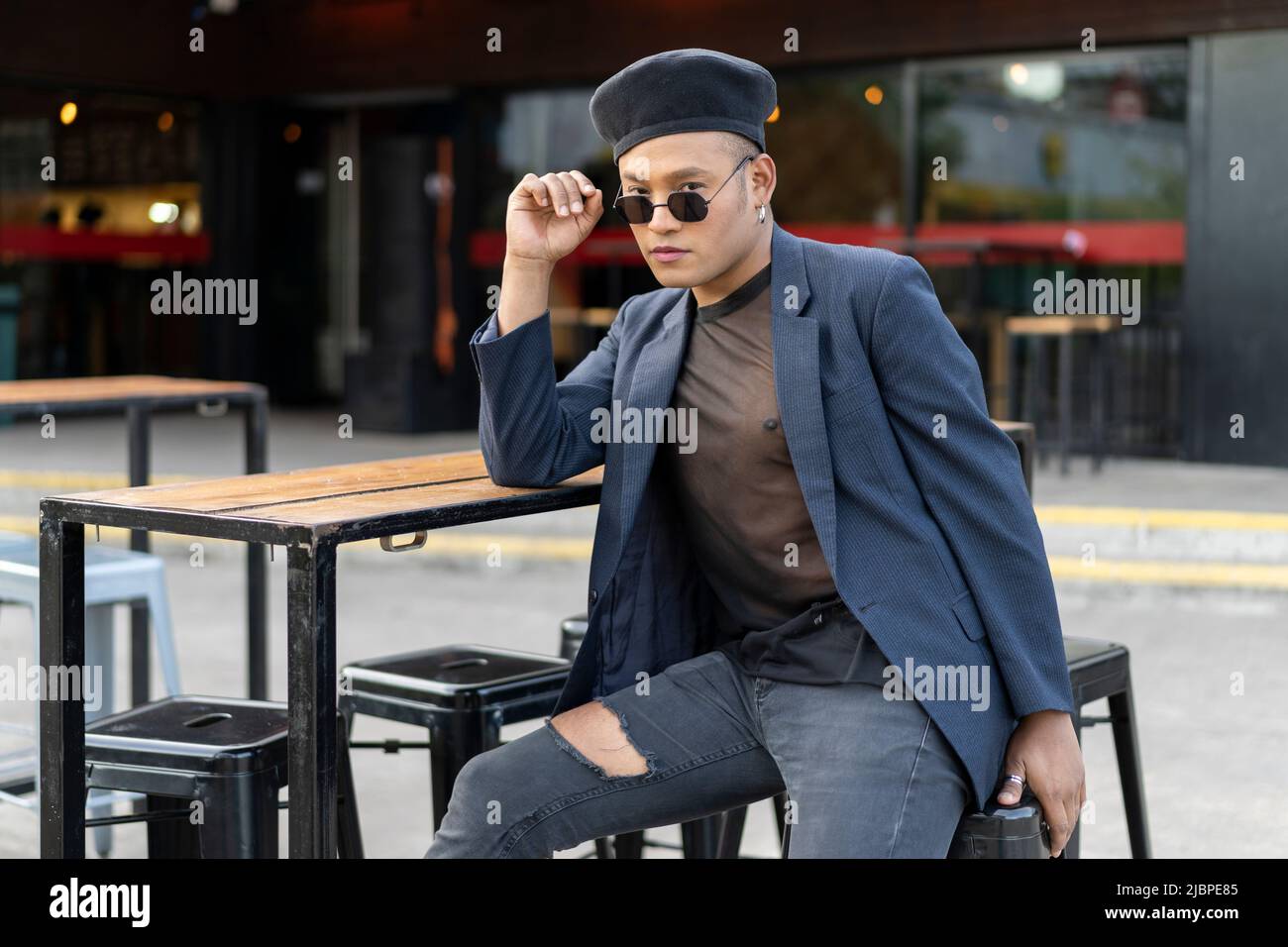 Latino gay maschio con trucco indossando cappello di moda in posa per strada Foto Stock