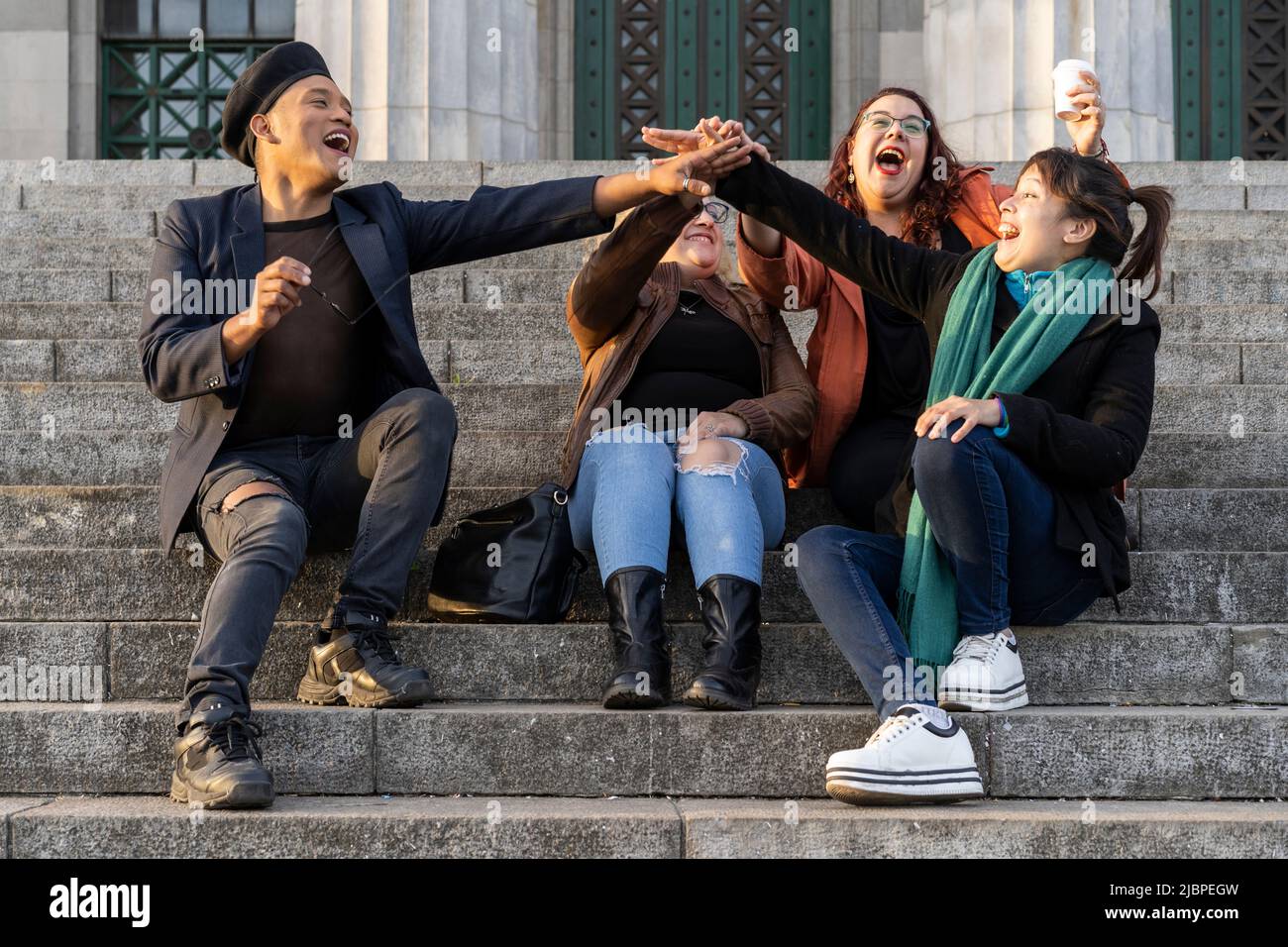Gruppo multietnico di amici seduti su alcune scale che si divertono a chiacchierare e a ridere Foto Stock