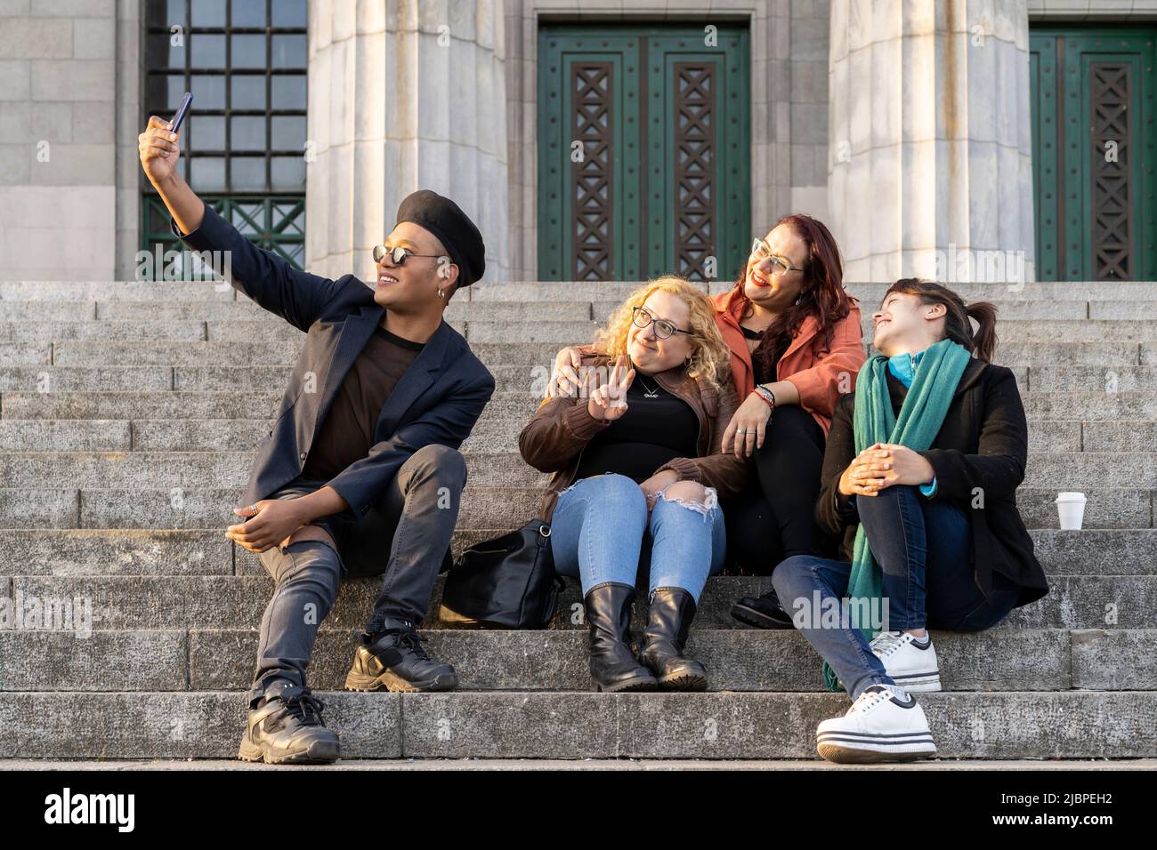 Gruppo multietnico di amici seduti su alcune scale che si divertono a chiacchierare, ridere e scattare foto Foto Stock