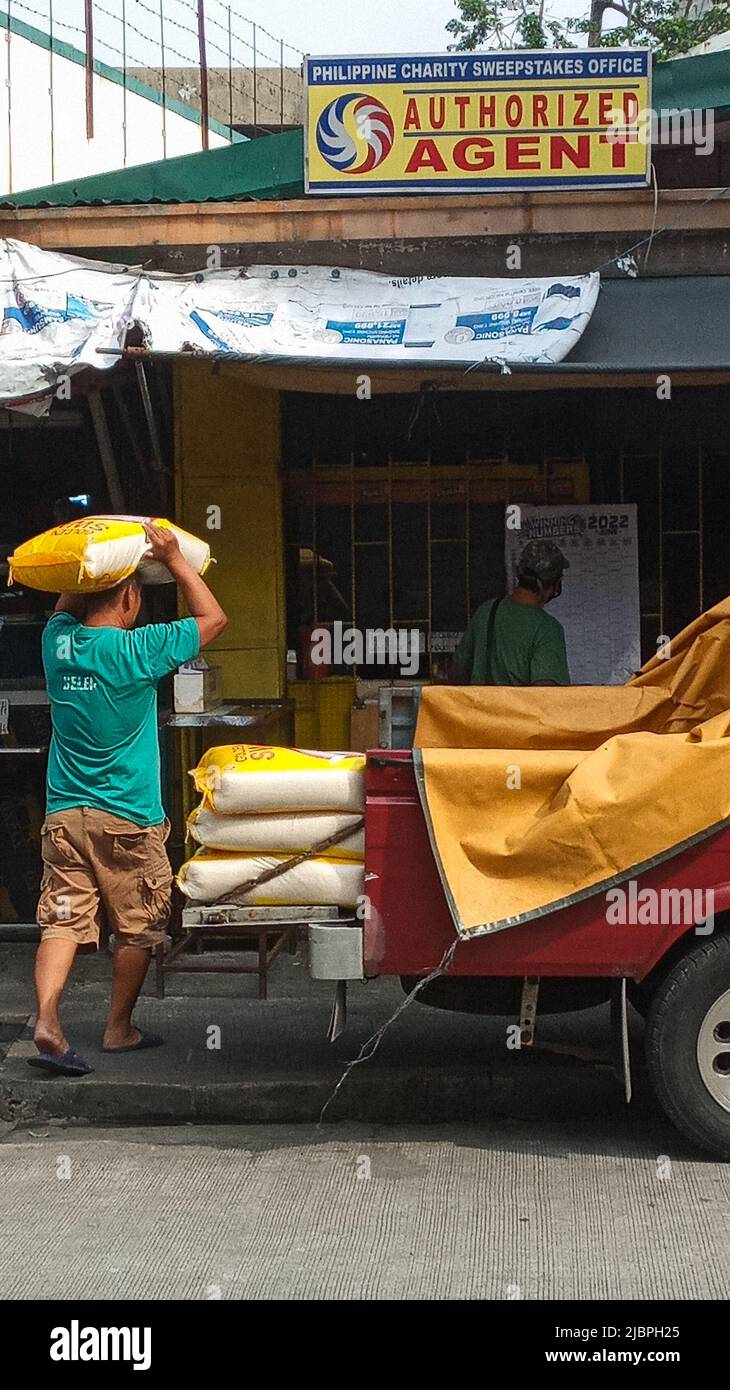 8 giugno 2022, Mandaluyong City, National Capital Region, Filippine: Una macina di lavoratori al mattino davanti a un negozio di lotterie. Questi facchini camion consegnano il sacco di riso in chili a questo negozio a doppio scopo. Un negozio sia per lotterie di beneficenza che per cereali di riso. Il presidente filippino entrante ha promesso un Ã¢''šÂ±20 ogni chilo di riso che è inferiore a 50Ã‚Â¢. Se da un lato Ã¢''šÂ±20 sarebbe un grande vantaggio per i consumatori pubblici, ma non per i nostri coltivatori di riso e lavoratori dell' industria del riso. Sembra che il duro lavoro non vi dà quella ricompensa ed è per questo che molti filippino provano la loro fortuna sulla vittoria a Foto Stock