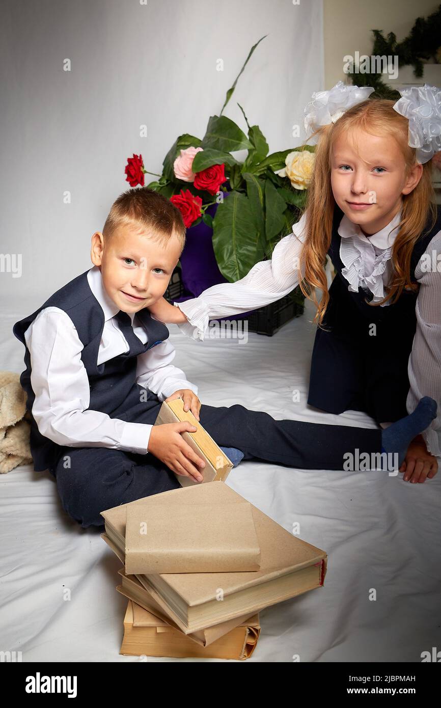 Ragazza e ragazzo che sono bambini elementari in uniforme divertirsi con il libro. Fratello e sorella il 1 settembre in Russia. Studentessa e scolaretto Foto Stock