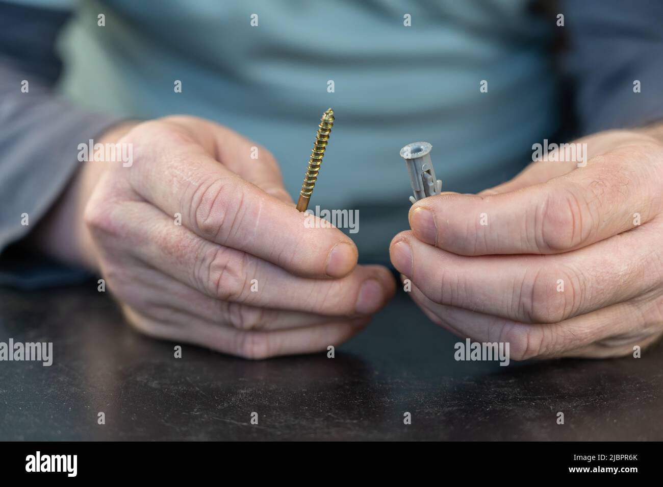 Un maschio per adulti trattiene una vite di tipo L con un perno di riferimento. Per il montaggio su pareti, soffitti e altre superfici viene utilizzata una vite con gancio. Primo piano. Sele Foto Stock