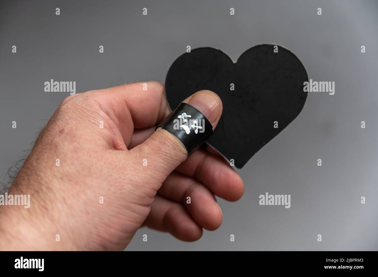L'uomo di mezza età tiene in mano il cuore nero. La falance del pollice è avvolta in nastro elettrico nero. Un volto triste con le grazie incrociate è disegnato o Foto Stock