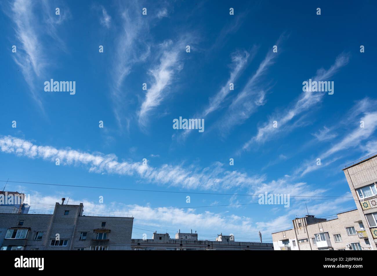 Inusuali nuvole sulla città. Strisce bianche di nuvole nel cielo estivo. Appartamenti in mattoni con finestre e balconi. Gli uccelli volano in alto nel cielo. Selez Foto Stock