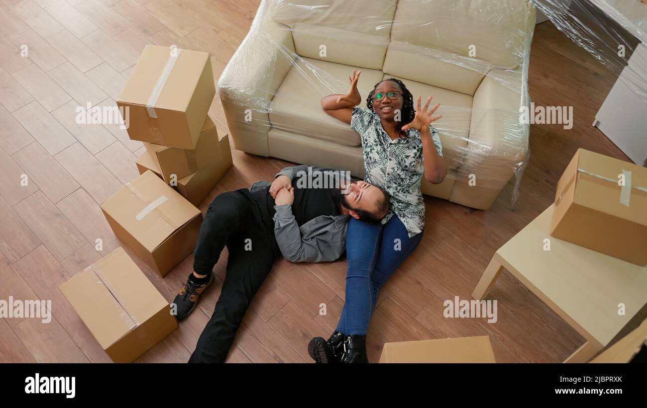 I partner sposati si sentono stanchi dopo essersi spostati in appartamento affittato insieme, seduti sul pavimento e parlando di futura famiglia. Sognare stile di vita e nuovi inizi. Scatto portatile. Vista dall'alto. Foto Stock