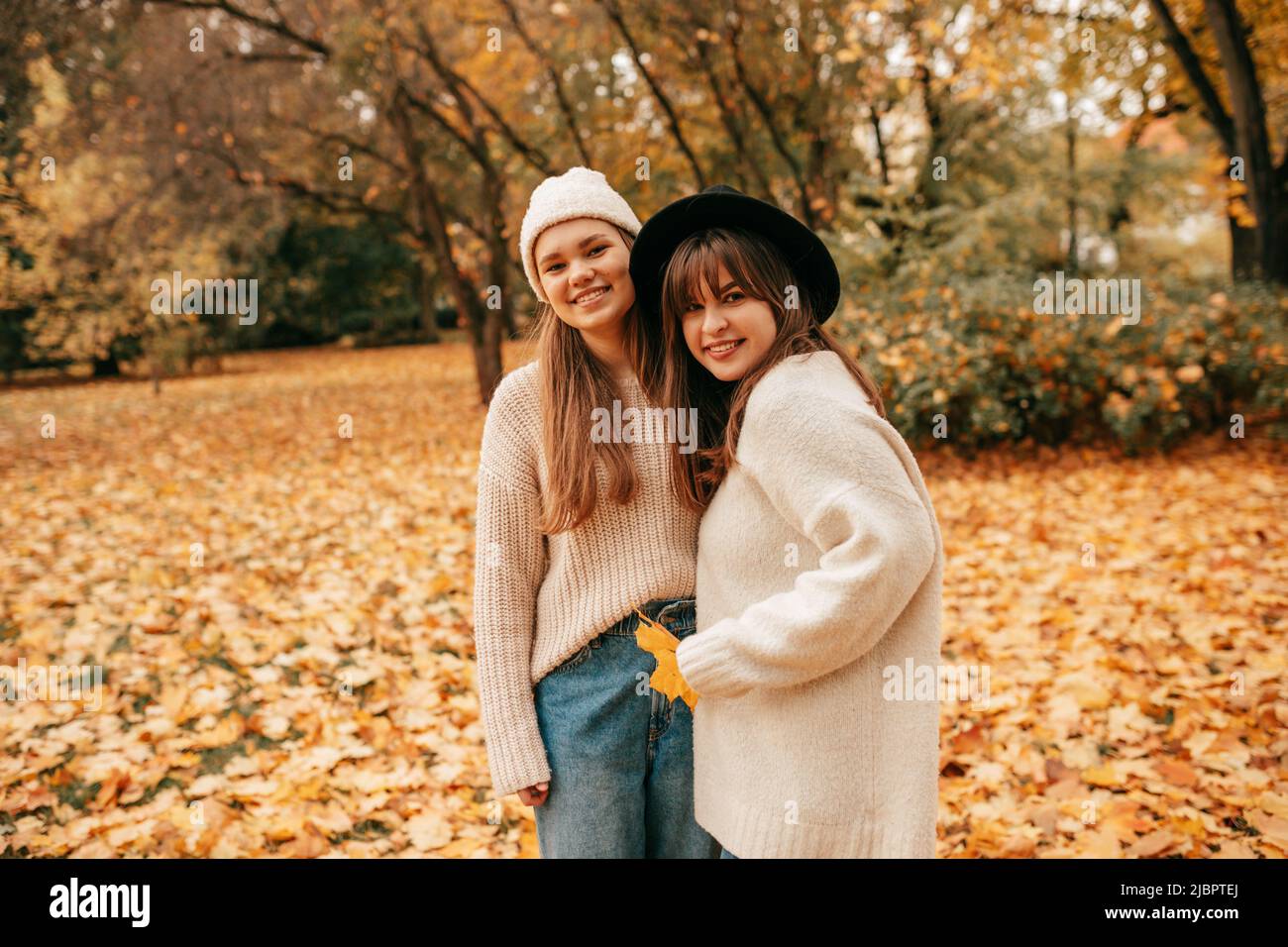 Due giovani donne affascinanti guardano alla macchina fotografica sorridendo e godendo di una calda giornata autunnale nel parco della città tra le foglie di arancio luminoso caduto. Buone vacanze. Bene Foto Stock
