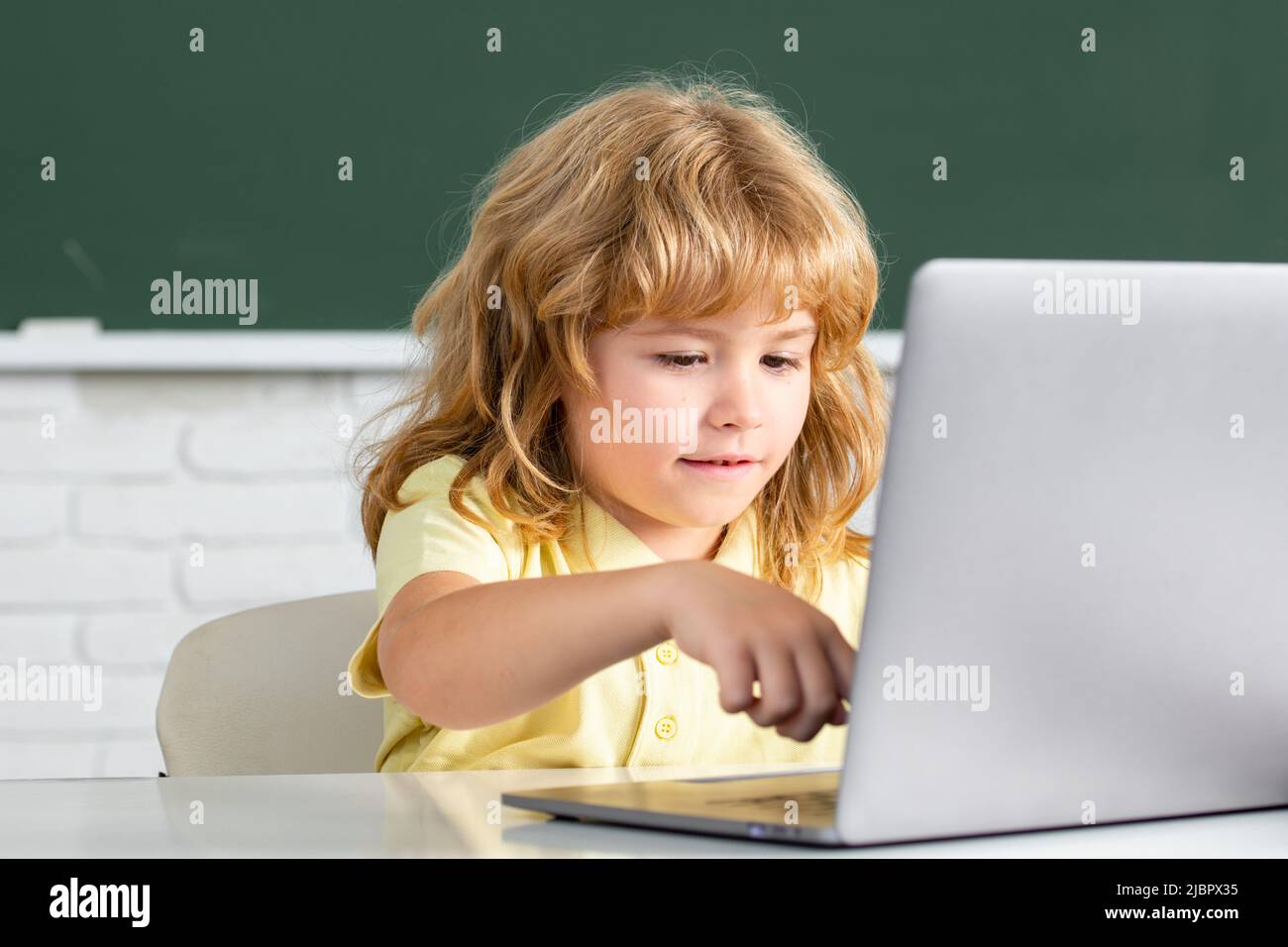 Bambino piccolo carino che usa il computer portatile, ragazzo che studia attraverso l'e-learning online. Piccolo amministratore di sistema divertente. Tecnologia di apprendimento online. Foto Stock