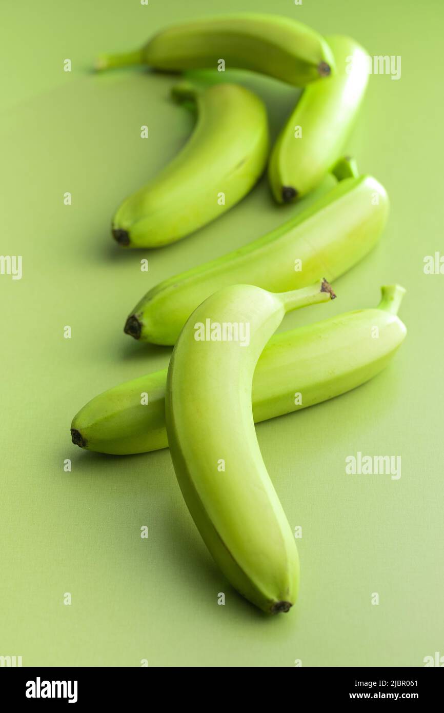 Banane verdi non mature su un tavolo verde. Foto Stock