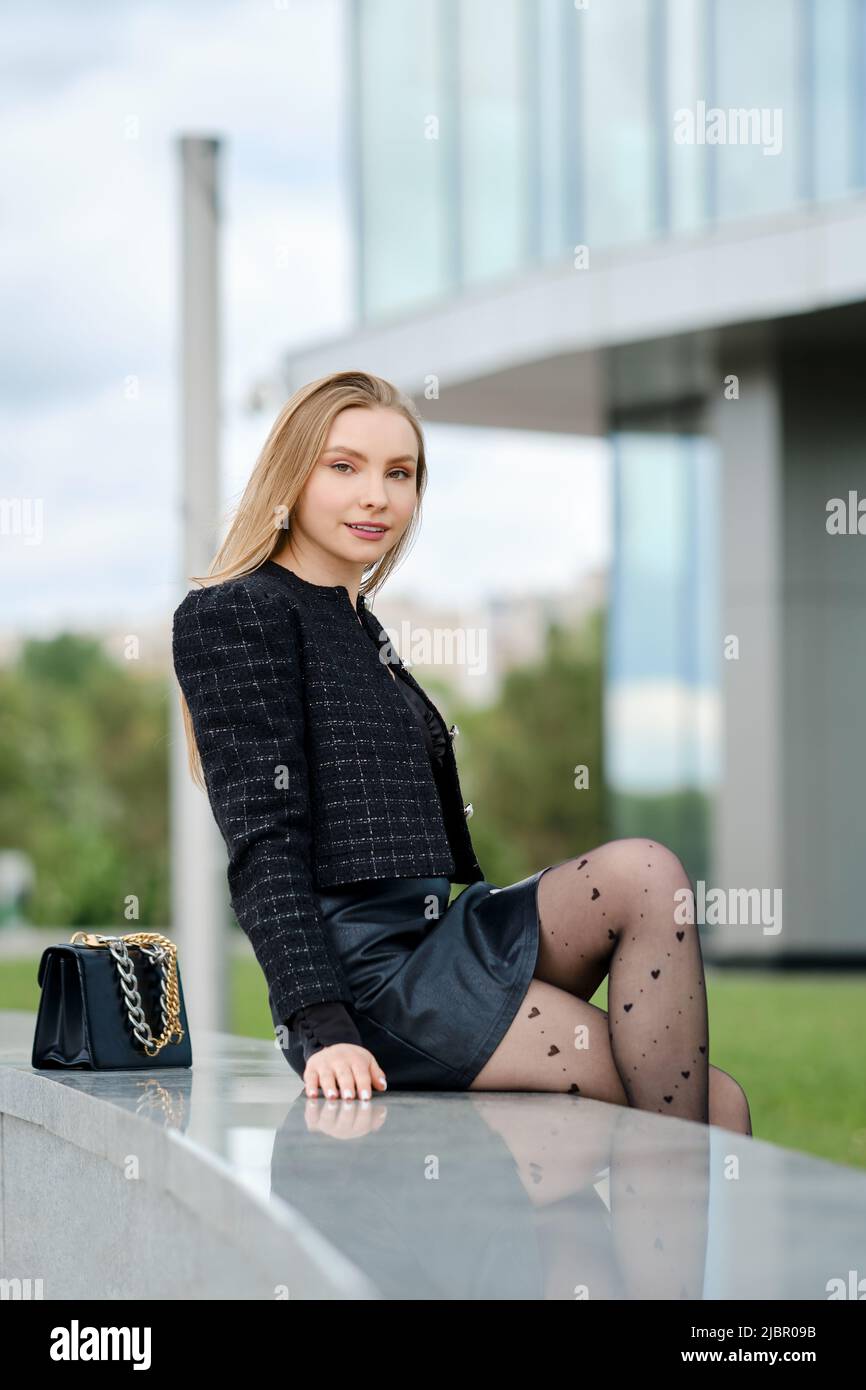 Bella giovane donna seduta su ringhiera di marmo vicino all'edificio degli uffici Foto Stock