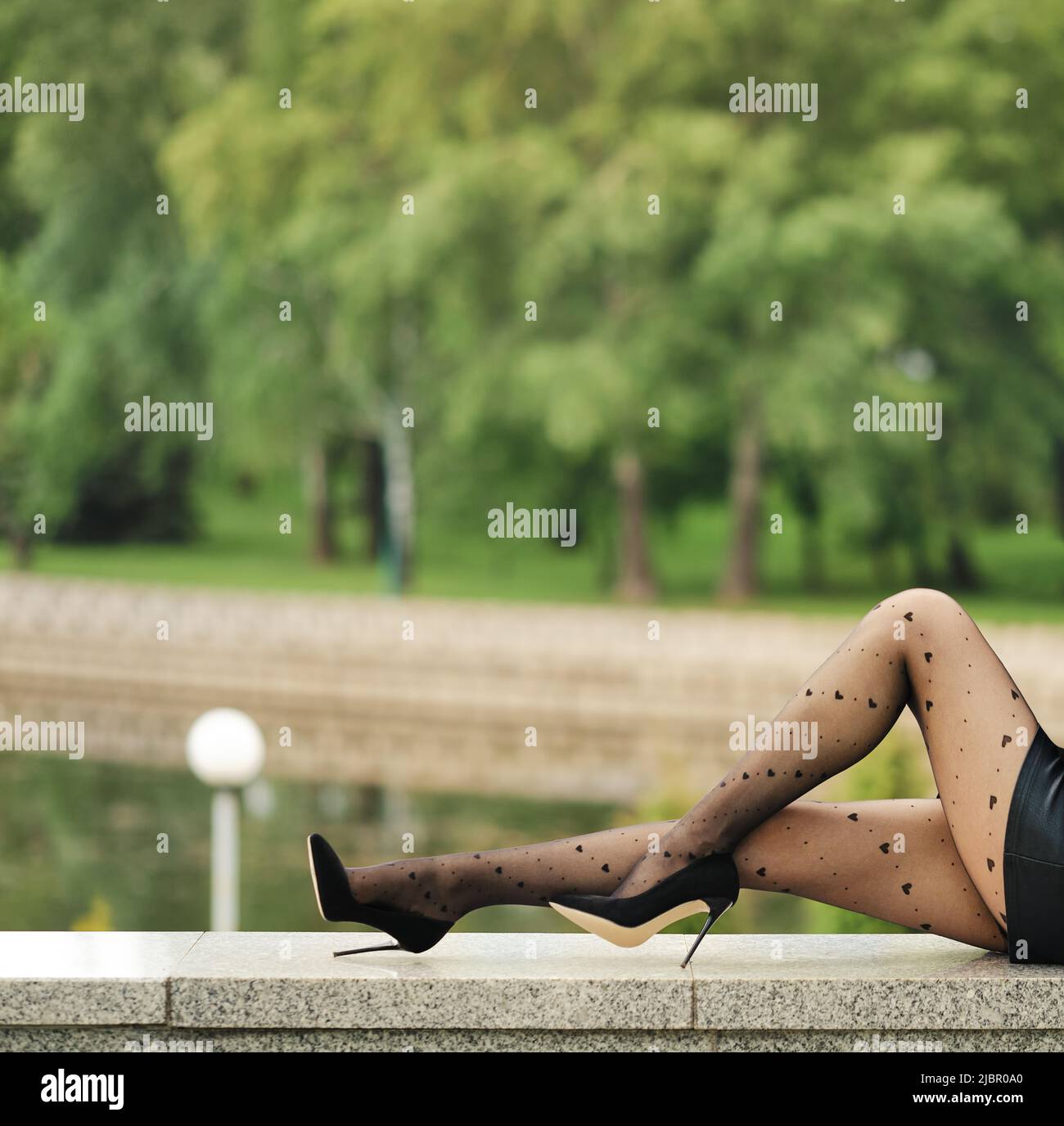 Gambe femminili sottili in collant con motivo a cuore in profilo con parco cittadino sullo sfondo Foto Stock