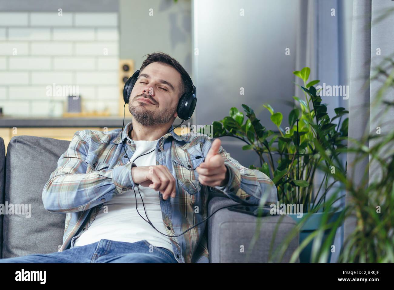 L'uomo stesso a casa ascolta la musica calma con le cuffie seduti sul divano rilassante Foto Stock