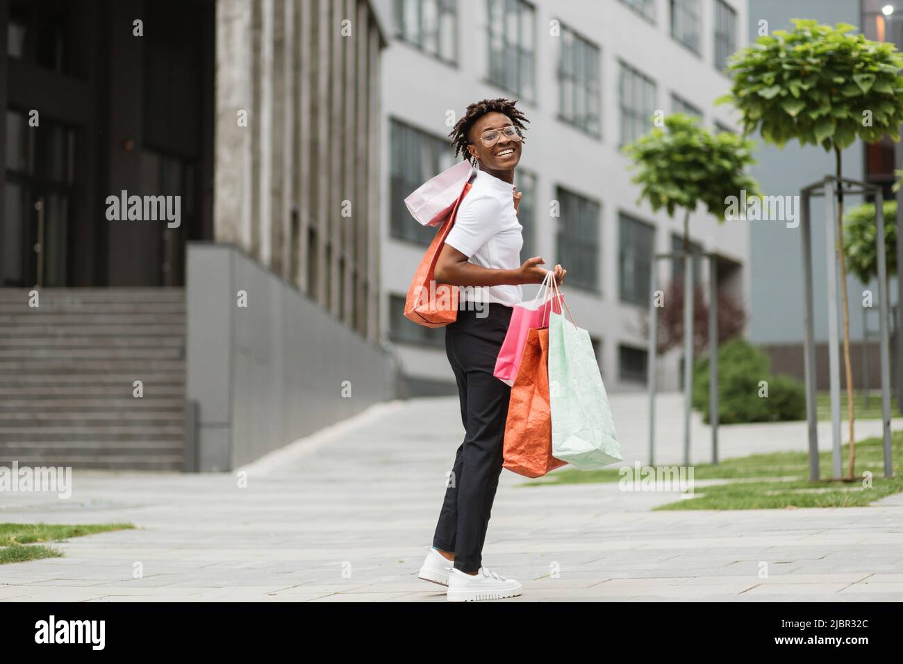 Outdoor full body fashion ritratto di donna afro-americana alla moda  indossando abiti alla moda, tenendo borse shopping colorate mentre si  cammina in strada della città moderna Foto stock - Alamy
