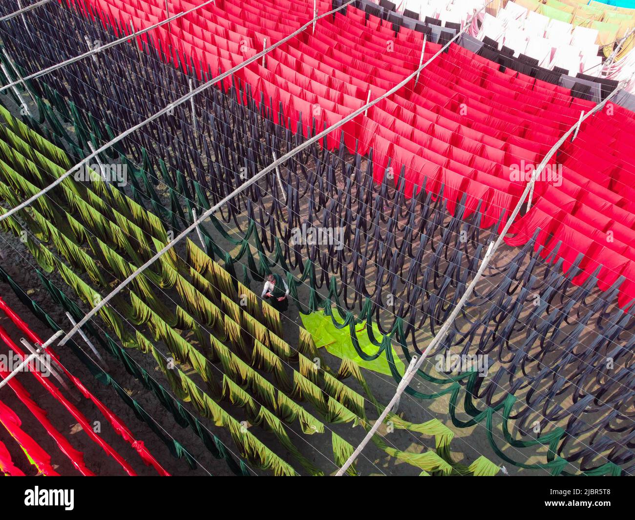 8 giugno 2022, Narayanganj, Dhaka, Bangladesh: I lavoratori appendono migliaia di metri di diversi tessuti colorati per asciugare in modo che possano essere fatti in t-shirt e giubbotti. I fili di ferro sono usati fra le strutture di bambù per generare le linee giganti di lavaggio per la parte finale del processo di tintura mentre i tessuti sono asciugati nel sole in Narayanganj, Bangladesh. Ciocche luminose di colore blu, rosa, arancione, rosso, viola, i panni colorati di giallo, magenta e verde sono appesi al di sopra del campo erboso in una scintillante rete di colori interbloccanti. Dopo cinque a sei ore al sole, il tessuto è utilizzato per fare abiti. Questo è il finale Foto Stock