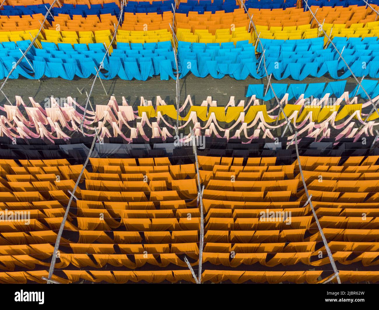 8 giugno 2022, Narayanganj, Dhaka, Bangladesh: I lavoratori appendono migliaia di metri di diversi tessuti colorati per asciugare in modo che possano essere fatti in t-shirt e giubbotti. I fili di ferro sono usati fra le strutture di bambù per generare le linee giganti di lavaggio per la parte finale del processo di tintura mentre i tessuti sono asciugati nel sole in Narayanganj, Bangladesh. Ciocche luminose di colore blu, rosa, arancione, rosso, viola, i panni colorati di giallo, magenta e verde sono appesi al di sopra del campo erboso in una scintillante rete di colori interbloccanti. Dopo cinque a sei ore al sole, il tessuto è utilizzato per fare abiti. Questo è il finale Foto Stock