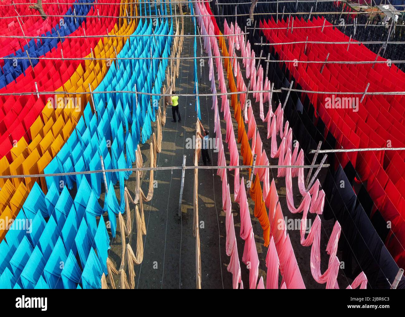 8 giugno 2022, Narayanganj, Dhaka, Bangladesh: I lavoratori appendono migliaia di metri di diversi tessuti colorati per asciugare in modo che possano essere fatti in t-shirt e giubbotti. I fili di ferro sono usati fra le strutture di bambù per generare le linee giganti di lavaggio per la parte finale del processo di tintura mentre i tessuti sono asciugati nel sole in Narayanganj, Bangladesh. Ciocche luminose di colore blu, rosa, arancione, rosso, viola, i panni colorati di giallo, magenta e verde sono appesi al di sopra del campo erboso in una scintillante rete di colori interbloccanti. Dopo cinque a sei ore al sole, il tessuto è utilizzato per fare abiti. Questo è il finale Foto Stock