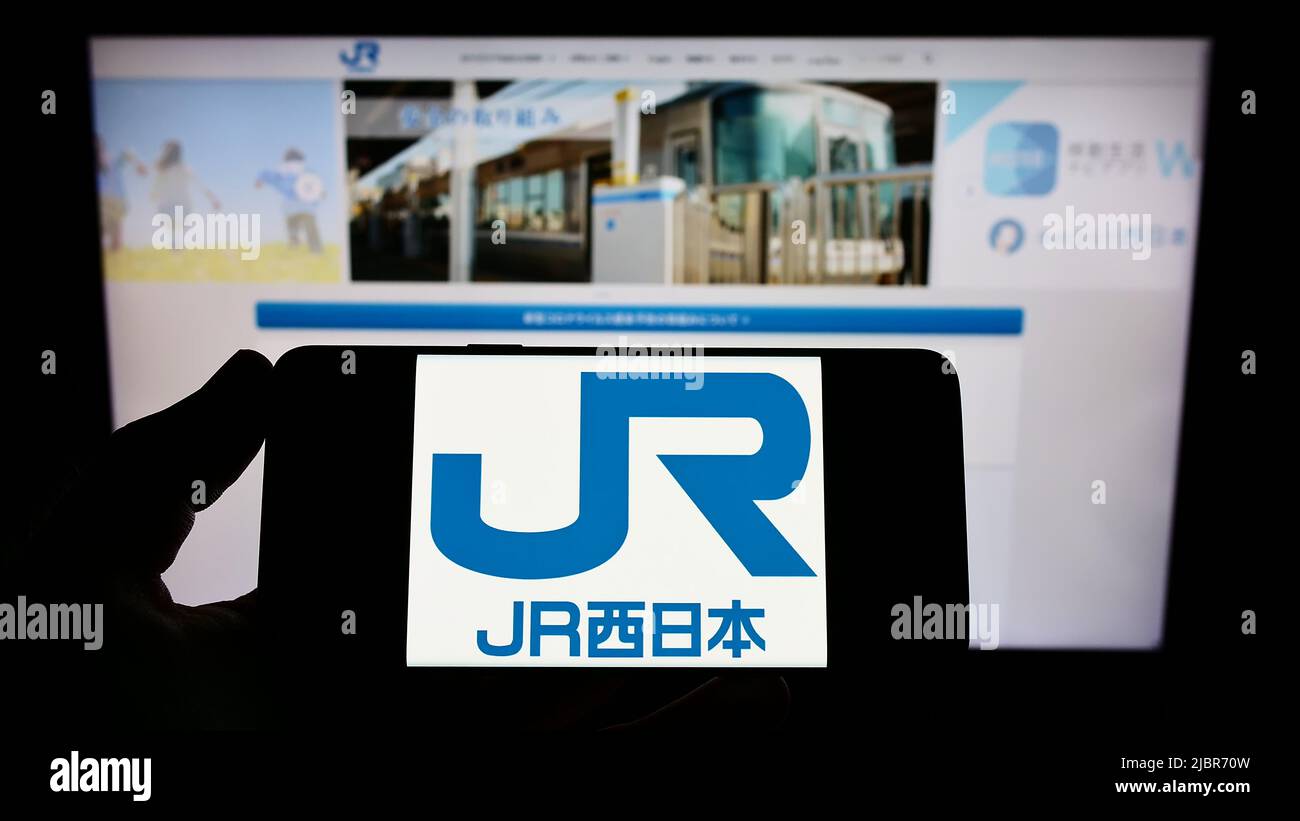 Persona che tiene uno smartphone con il logo della compagnia giapponese West Japan Railway (JR) sullo schermo di fronte al sito Web. Mettere a fuoco sul display del telefono. Foto Stock
