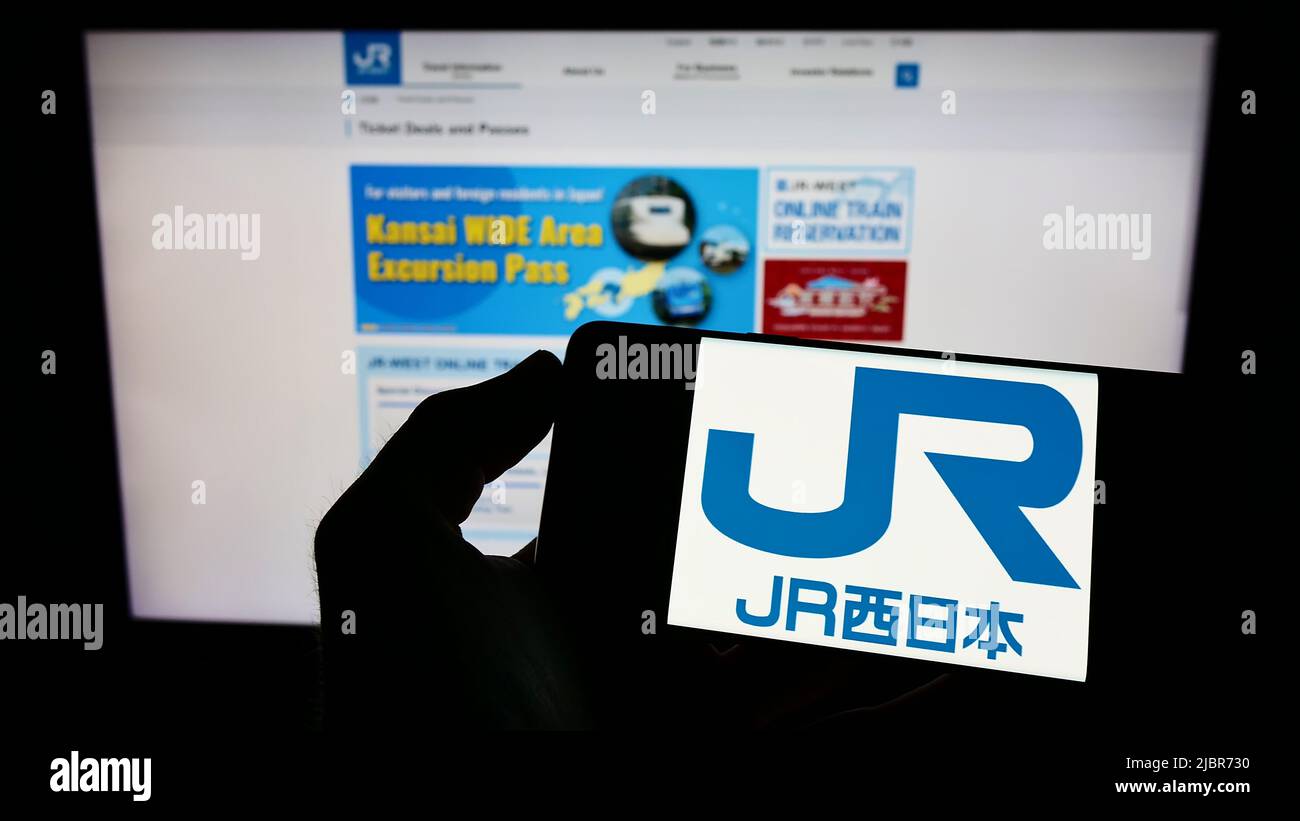 Persona che tiene il cellulare con il logo della compagnia giapponese West Japan Railway (JR) sullo schermo di fronte al sito web aziendale. Mettere a fuoco sul display del telefono. Foto Stock