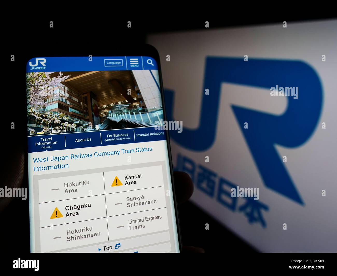 Persona che tiene il telefono cellulare con la pagina web della compagnia giapponese West Japan Railway (JR) sullo schermo di fronte al logo. Concentrarsi sul centro del display del telefono. Foto Stock