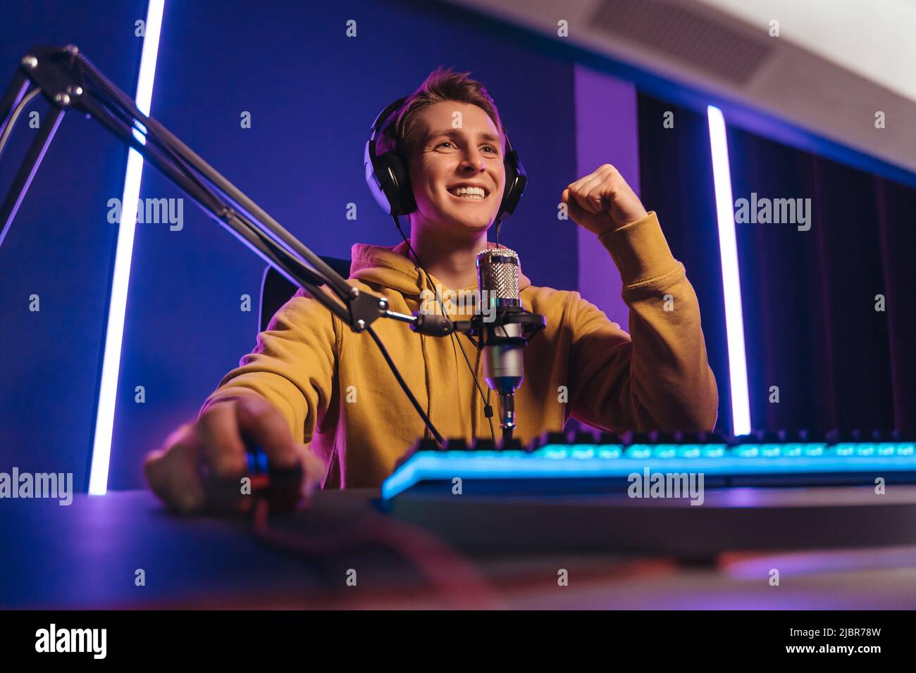 Il giocatore professionista di eSport si sente eccitato mentre gioca nel gioco di sport di cibernetica in linea, ha vinto il gioco ed allietato con le mani che si sentono, sorridenti, si sentono felici e felici con la sua vittoria. Dipendenza dal computer, ossessione per i giochi Foto Stock