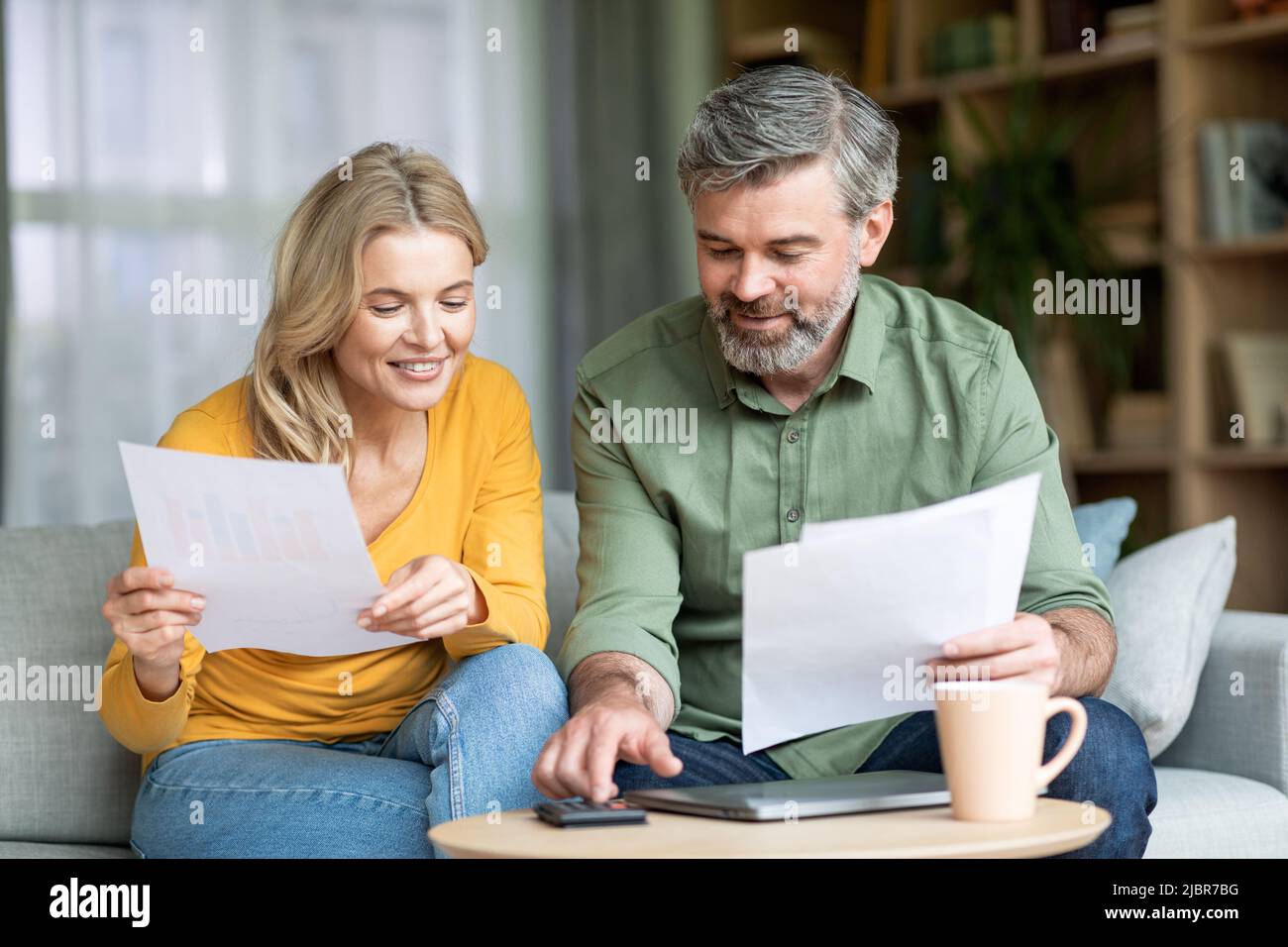 Coniugi di mezza età che controllano la documentazione finanziaria mentre pianificano il budget familiare a casa Foto Stock