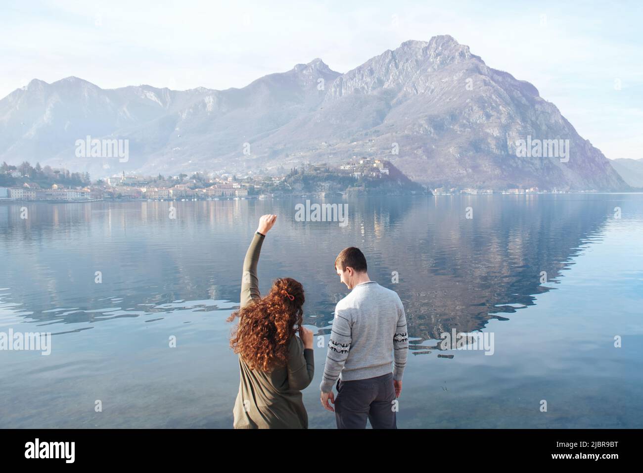 Soft Focus, coppia con vista posteriore che gode di una data romantica sulle rive del Lago di Lecco, Italia. Persone innamorate sullo sfondo di montagne, acqua all'aperto. Relazioni romantiche, avventure, vacanze. Spazio di copia Foto Stock