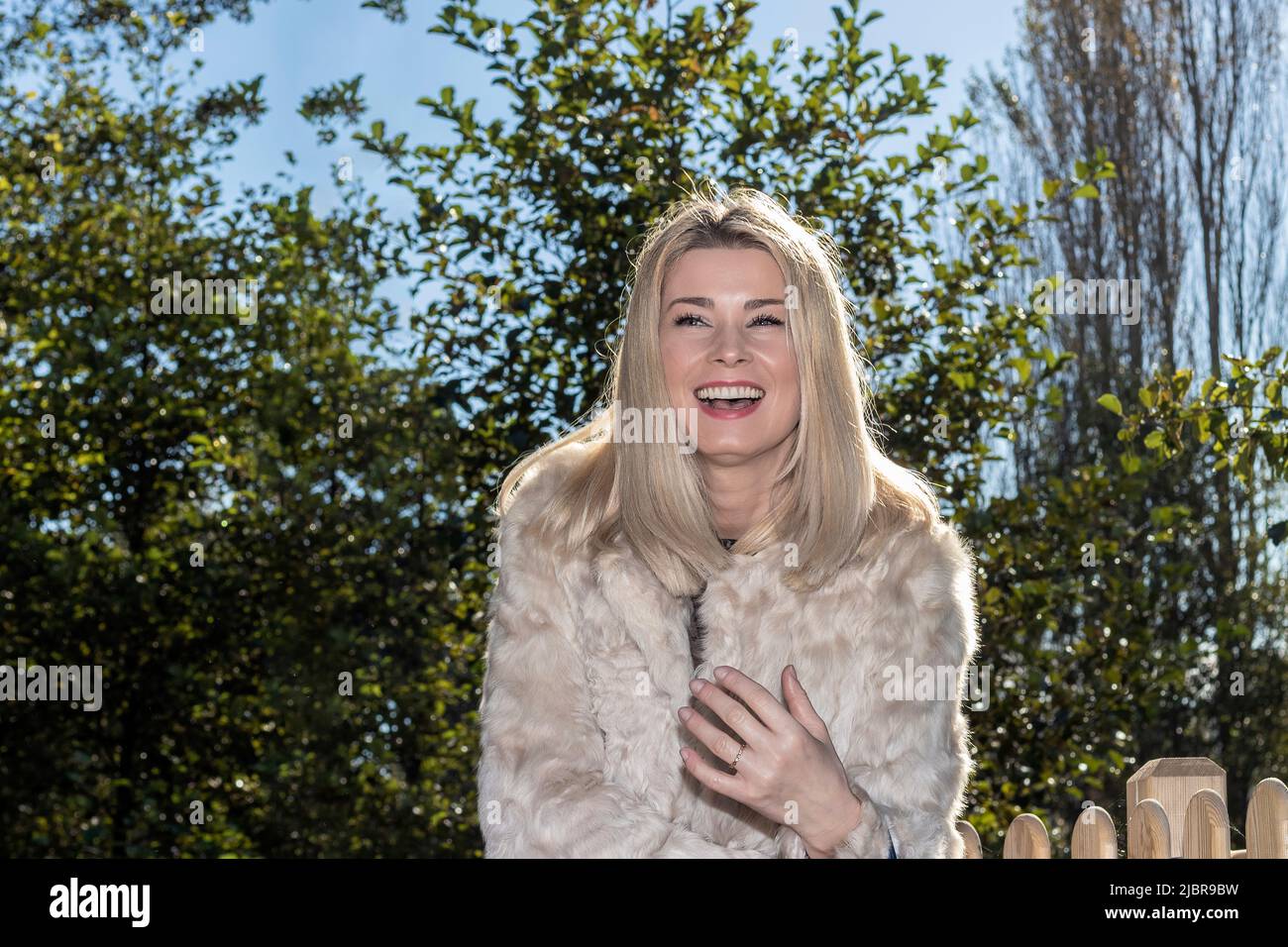 bella donna bionda ridendo gioiosamente in un parco in una giornata d'inverno soleggiata Foto Stock