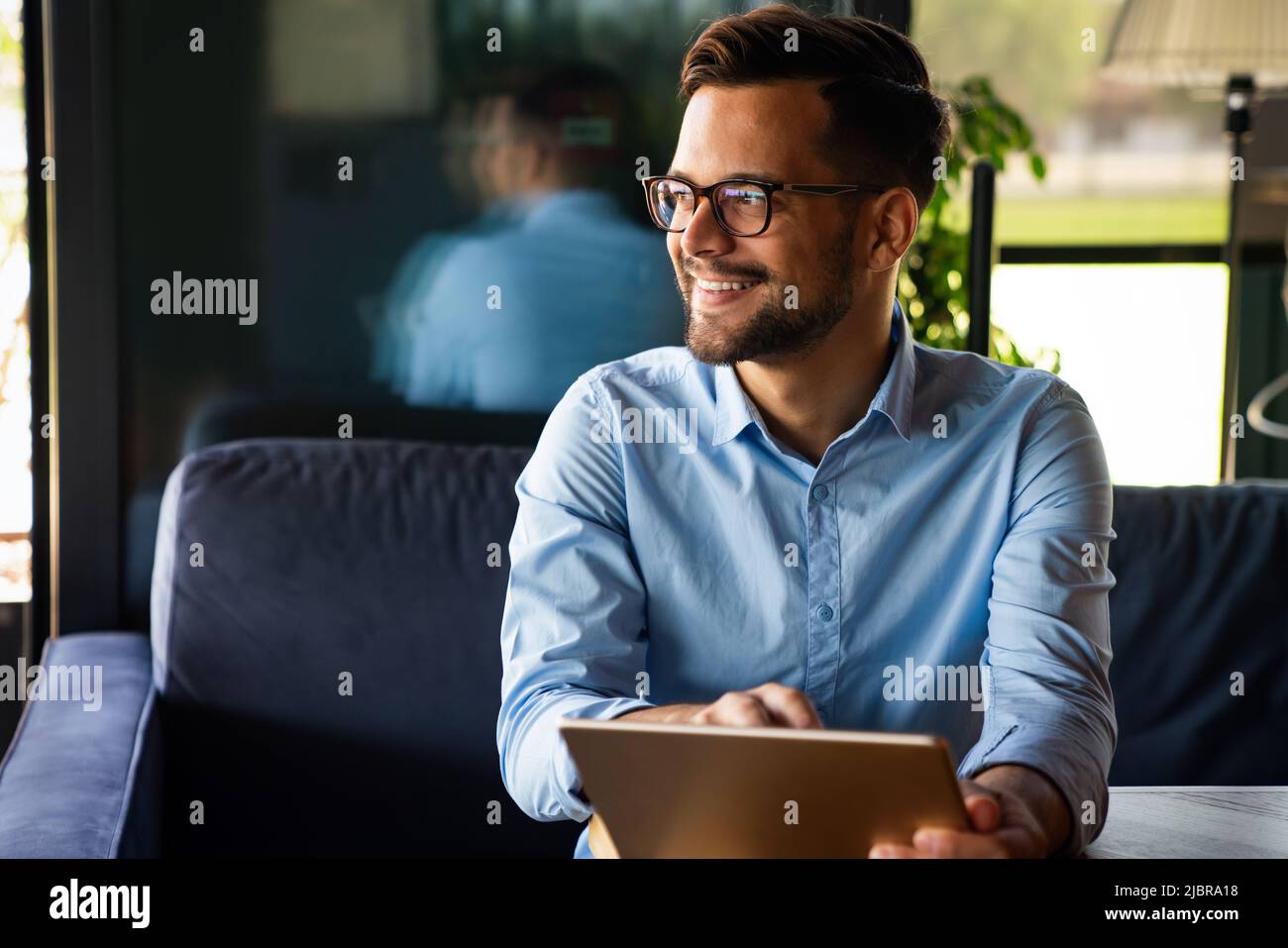 Giovane uomo d'affari sorridente di successo, imprenditore in una suite aziendale formale che lavora su tablet Foto Stock