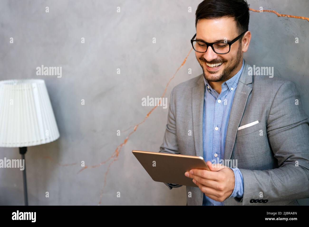 Giovane uomo d'affari sorridente di successo, imprenditore in una suite aziendale formale che lavora su tablet Foto Stock