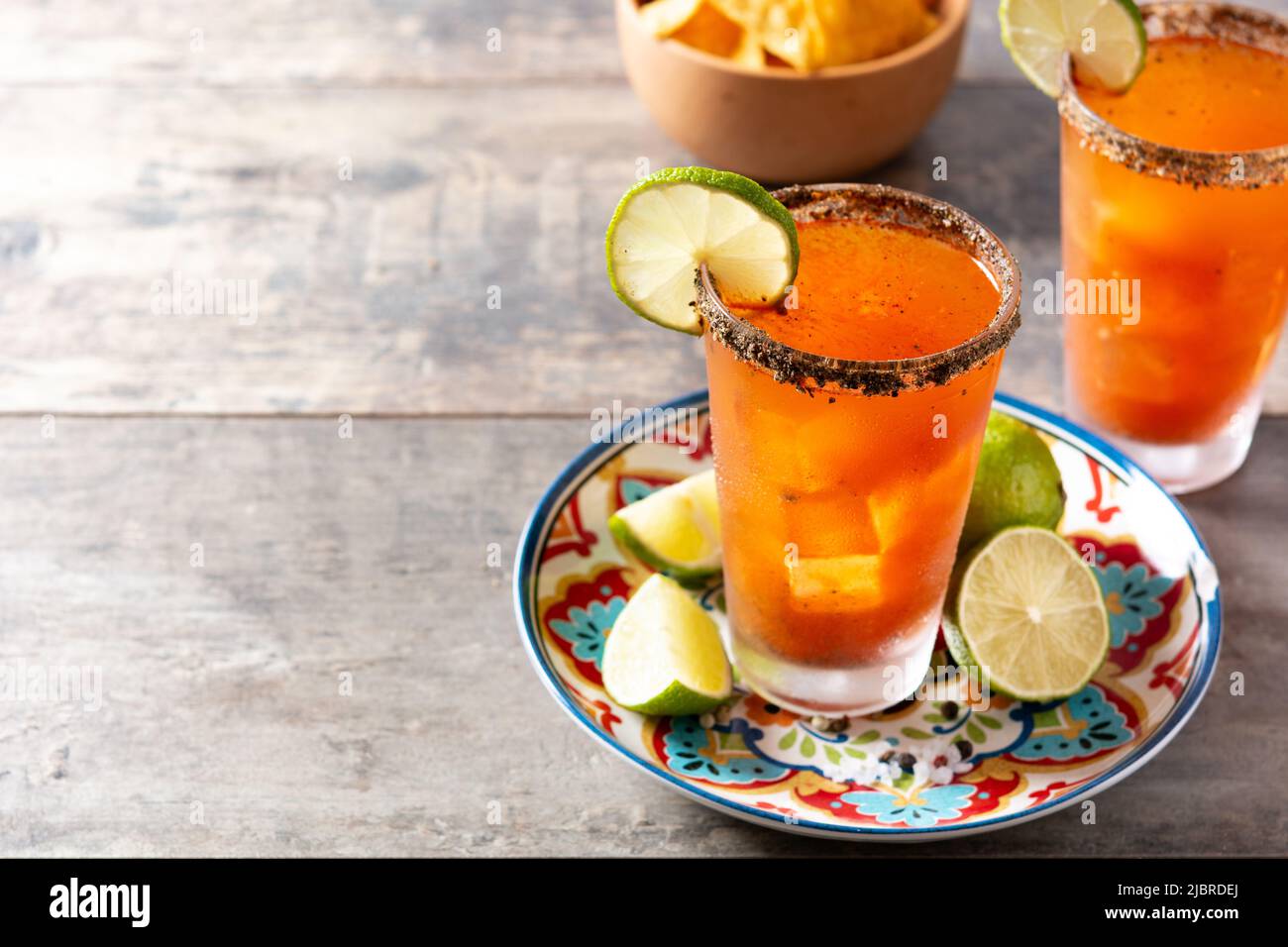 Cocktail michelada fatto in casa con birra, succo di lime, salsa calda, bordo salato e succo di pomodoro su tavola di legno Foto Stock