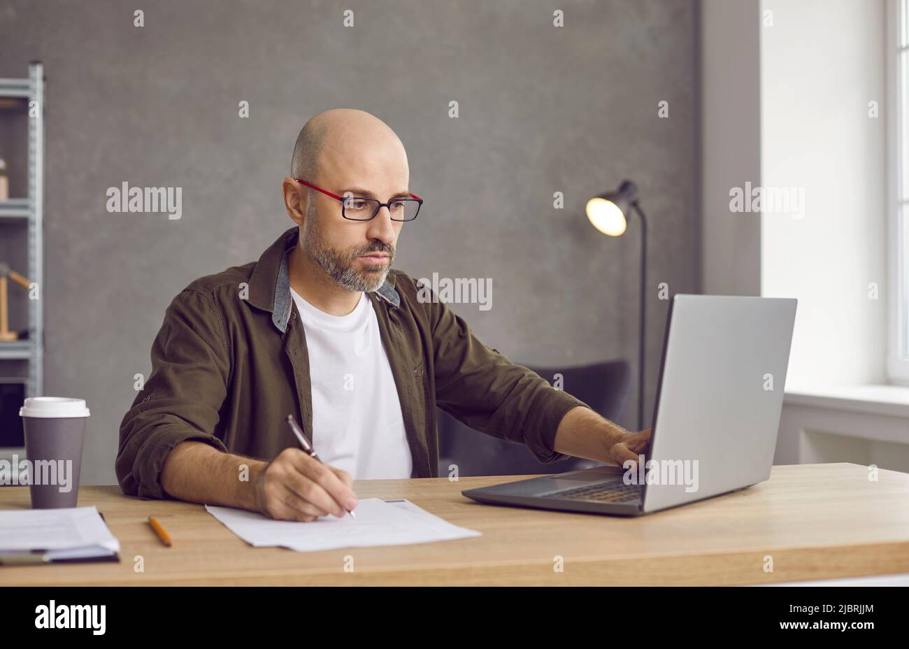 Uomo seduto al tavolo in ufficio, che lavora su un computer portatile e che scrive le informazioni Foto Stock