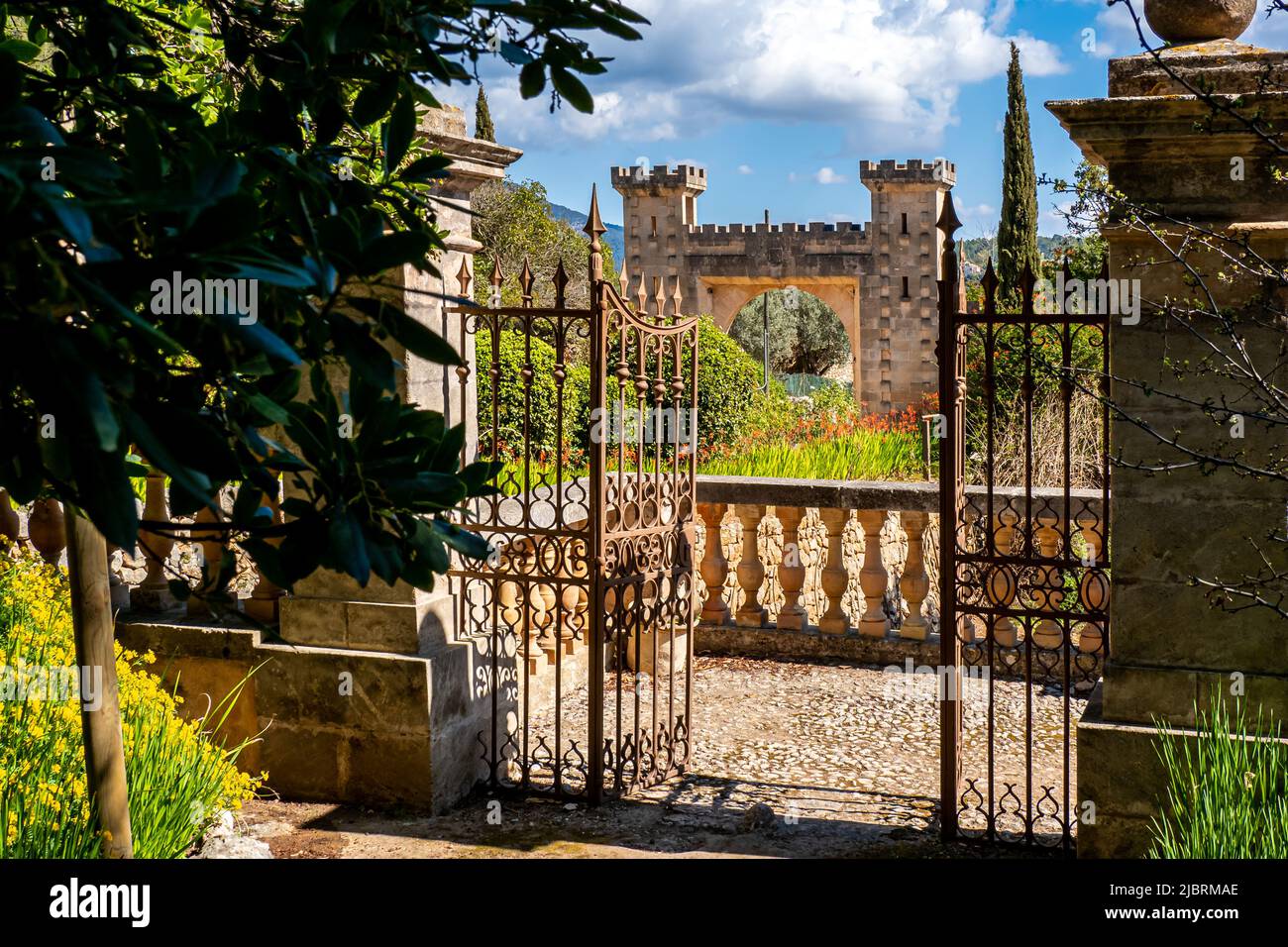Una recinzione in ferro arrugginita di fronte ad una ringhiera in pietra conduce ad un giardino con piante verdeggianti che circonda l'impressionante entrata di Raixa. Foto Stock