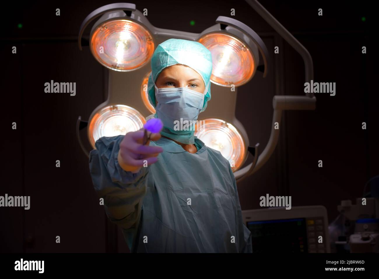 Una donna è vista in un teatro di funzionamento dell'ospedale. È completamente vestita come infermiera anestetica con una maschera facciale e indumenti chirurgici medici sterili. Foto Stock