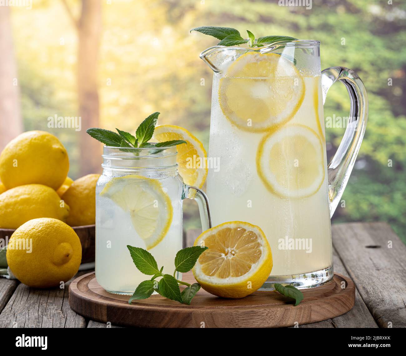 Bicchiere e caraffa di limonata con fette di limone e menta su un vecchio tavolo di legno con sfondo rurale estivo Foto Stock