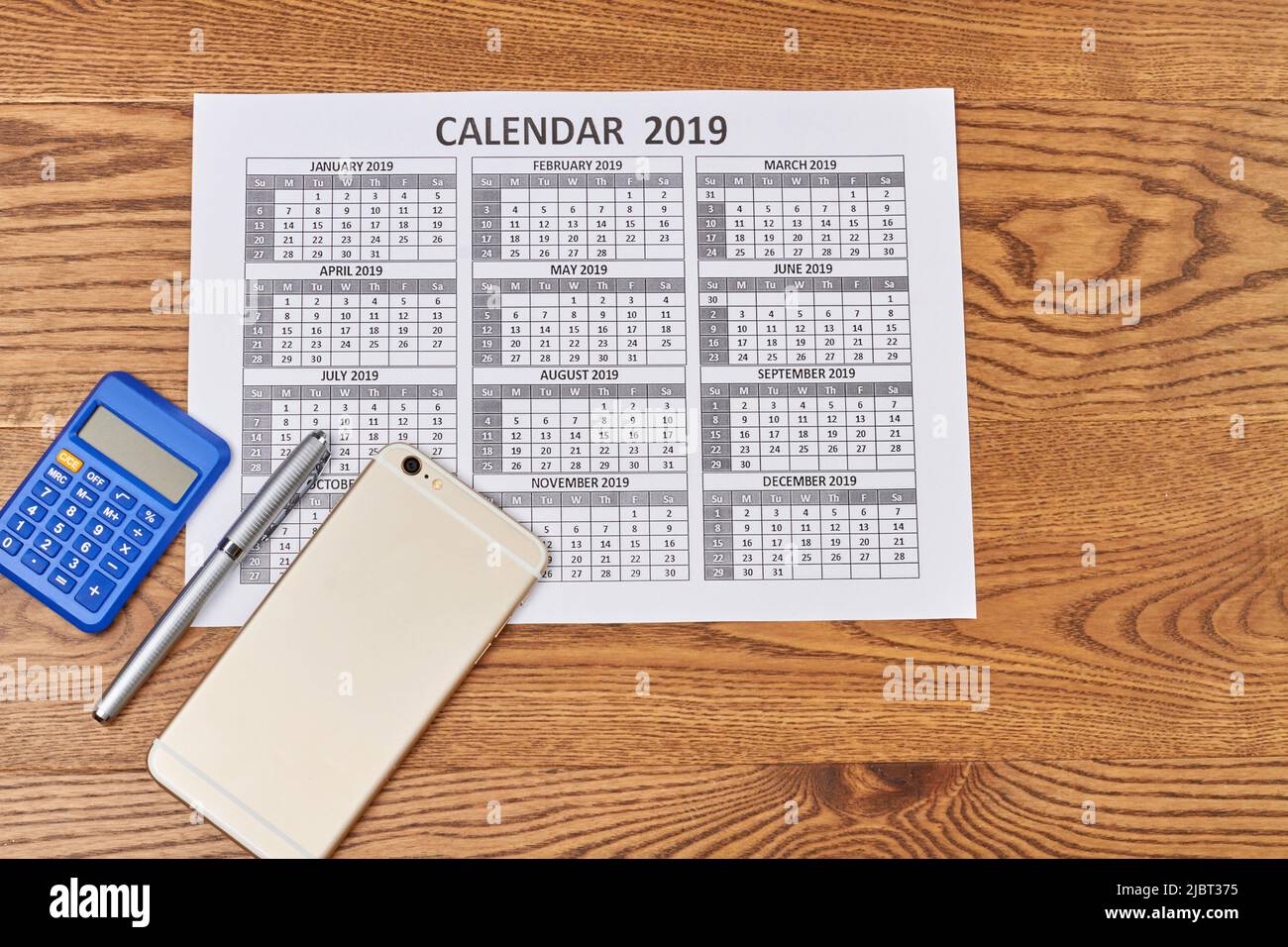 Calcolatrice piatta con penna e smartphone su scrivania in legno. Accessori per account business. Foto Stock