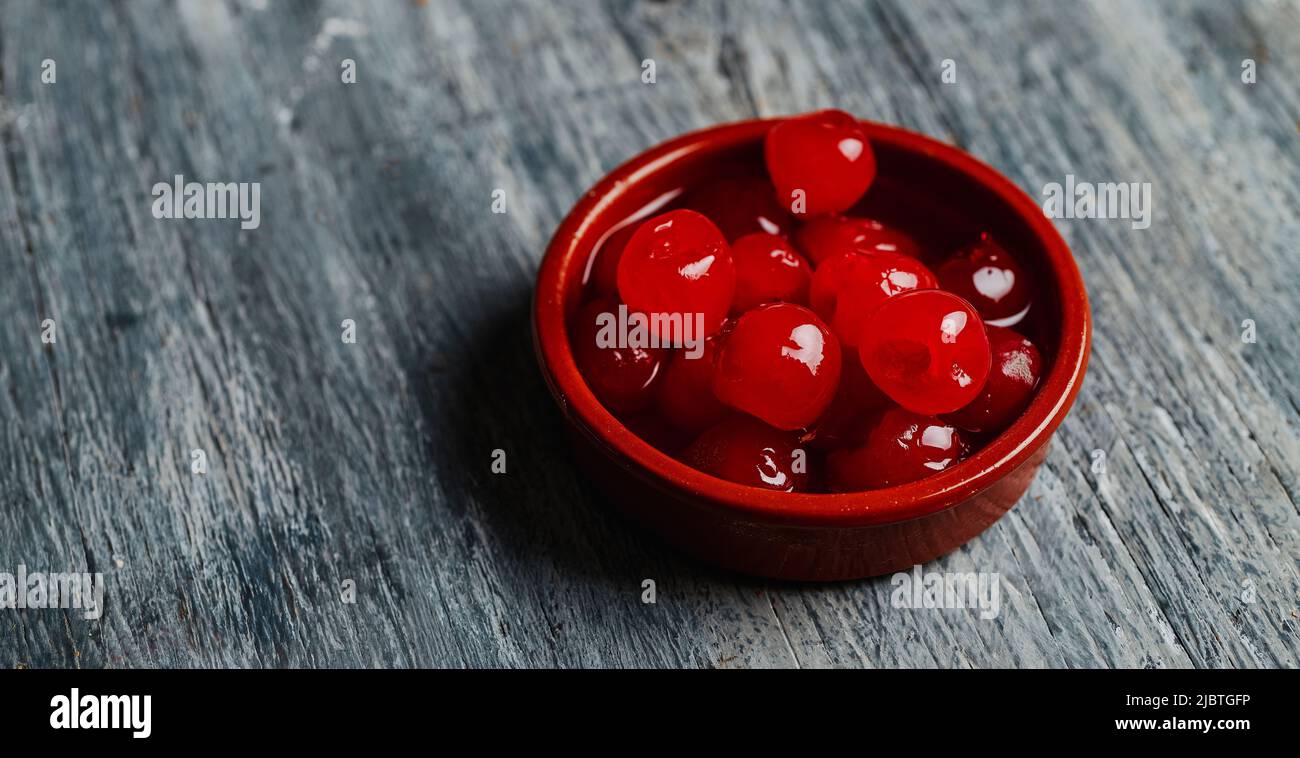 una ciotola di terracotta marrone con alcune ciliegie di maraschino, su un tavolo grigio rustico in legno, in formato panoramico da utilizzare come banner o testata web Foto Stock
